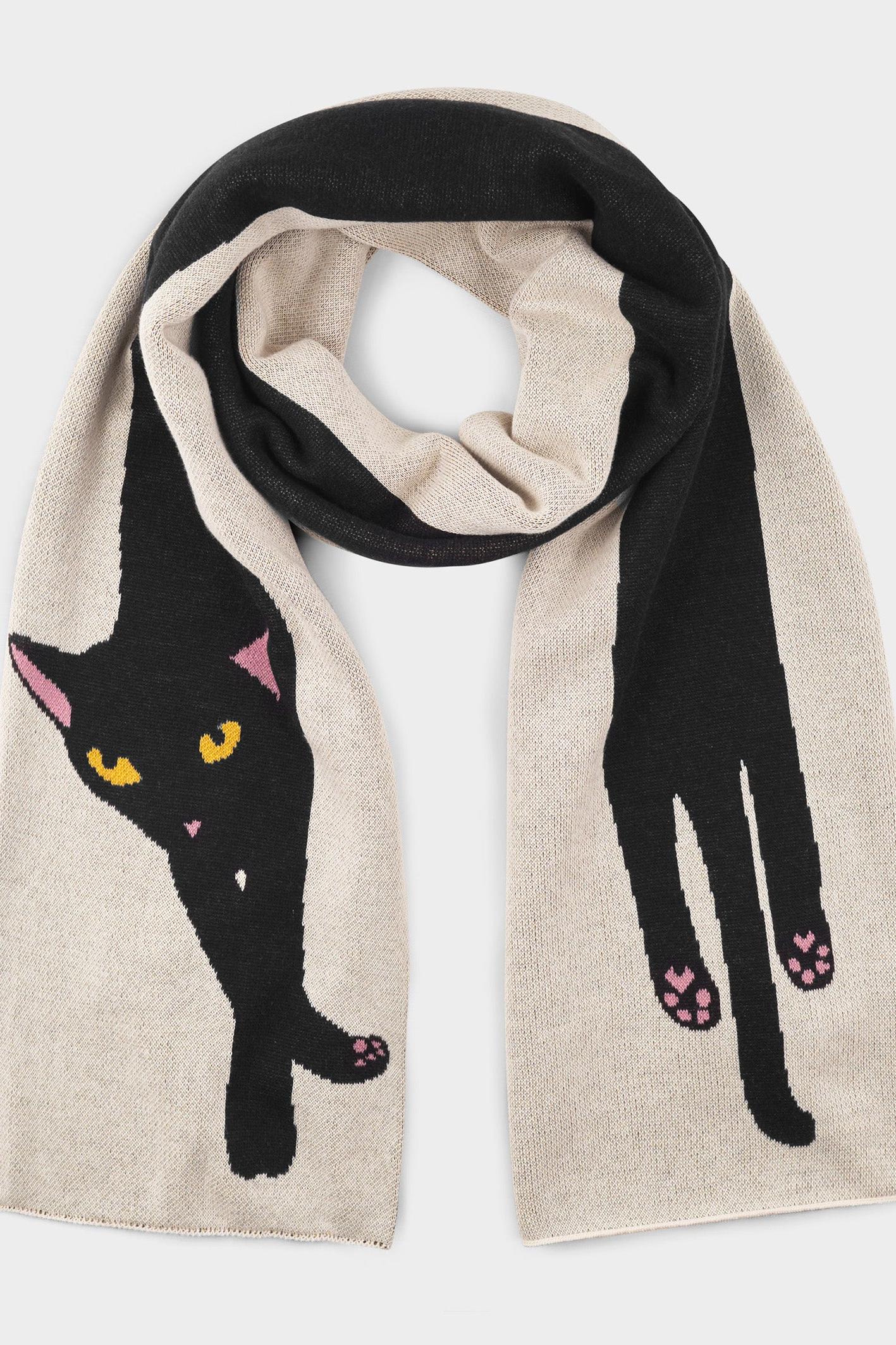 A beige knit scarf featuring a large black cat design with pink and yellow details, draped in a loop against a light gray background.
