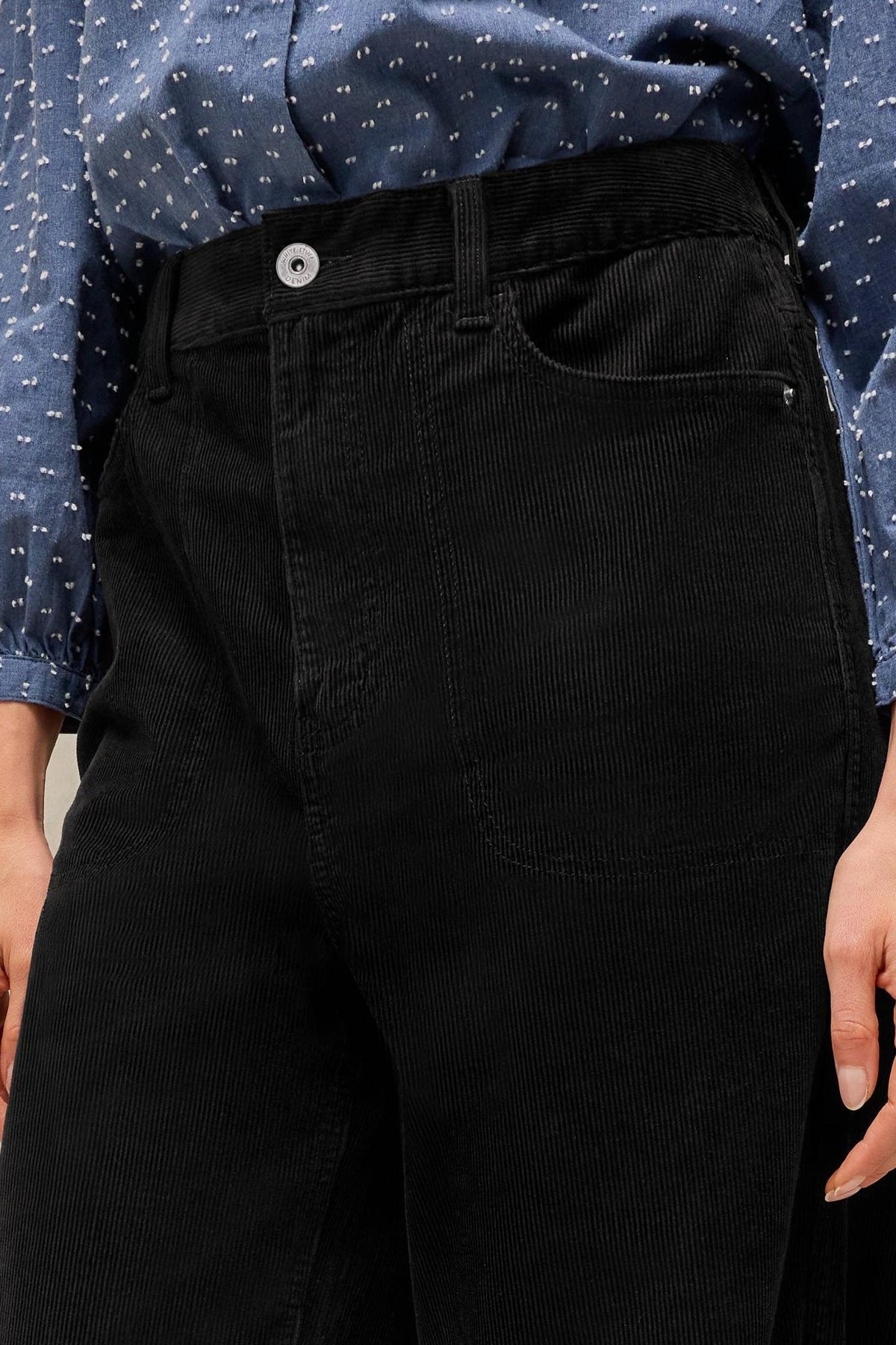 Close-up of black corduroy wide leg trousers by White Stuff paired with a blue patterned shirt.