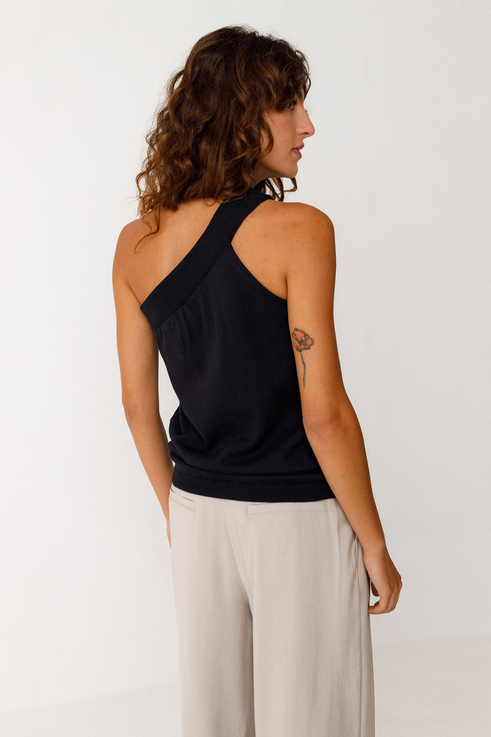 Woman wearing a black sleeveless top and beige pants against a white background