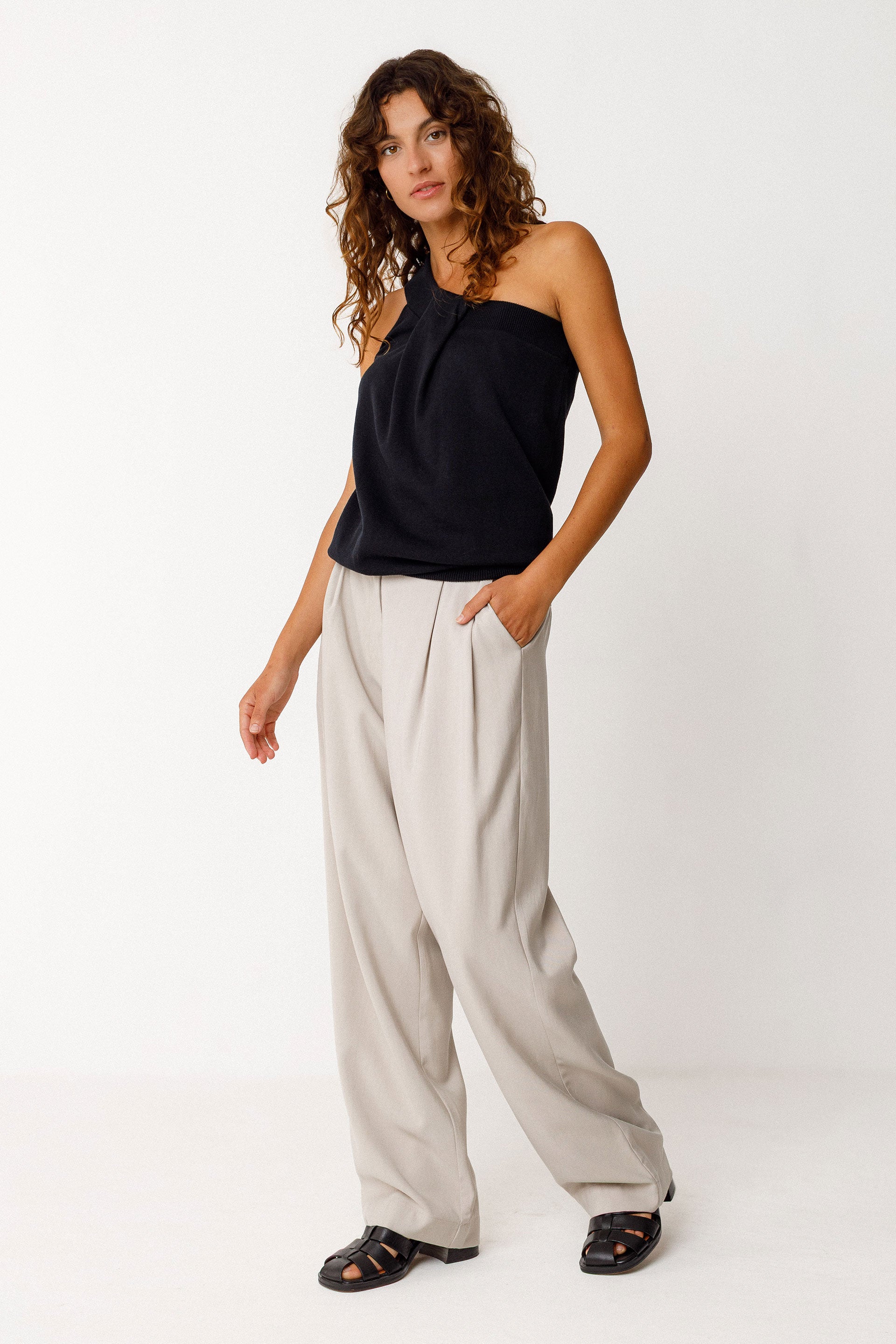 Woman wearing a black halter organic cotton top and beige wide-leg pants on a white background