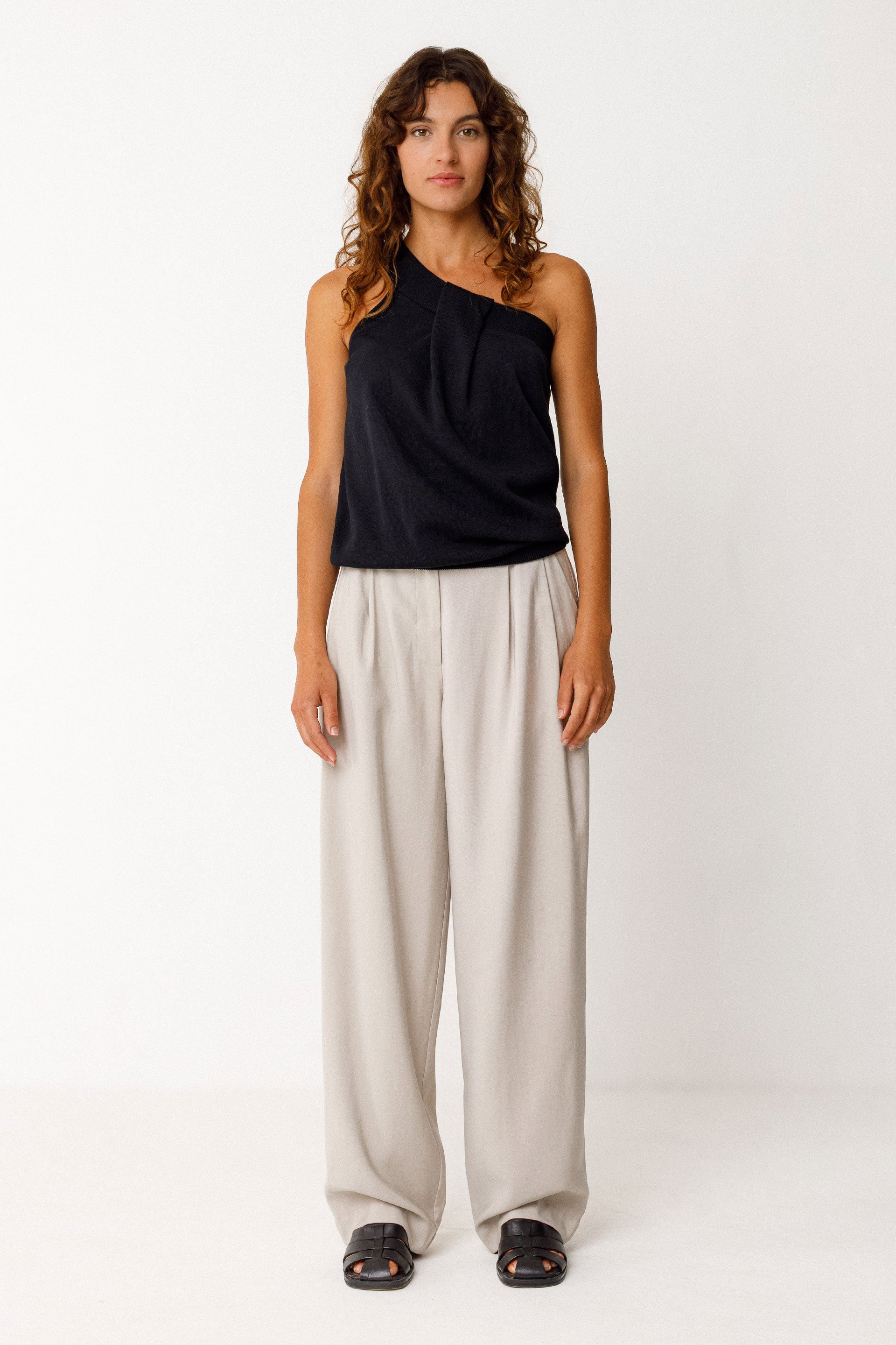 Woman wearing a black sleeveless top and beige wide-leg pants on a white background