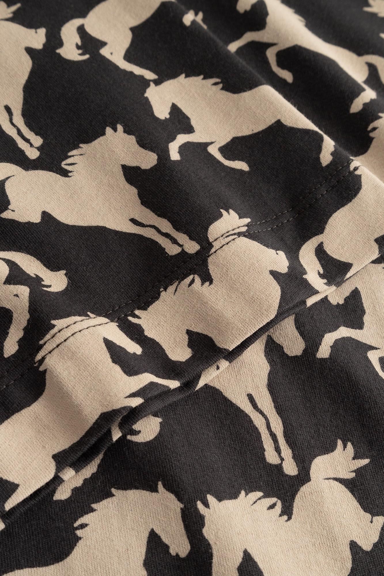 Close-up of a black fabric with a repeating beige horse silhouette print, showing the material texture and stitching.