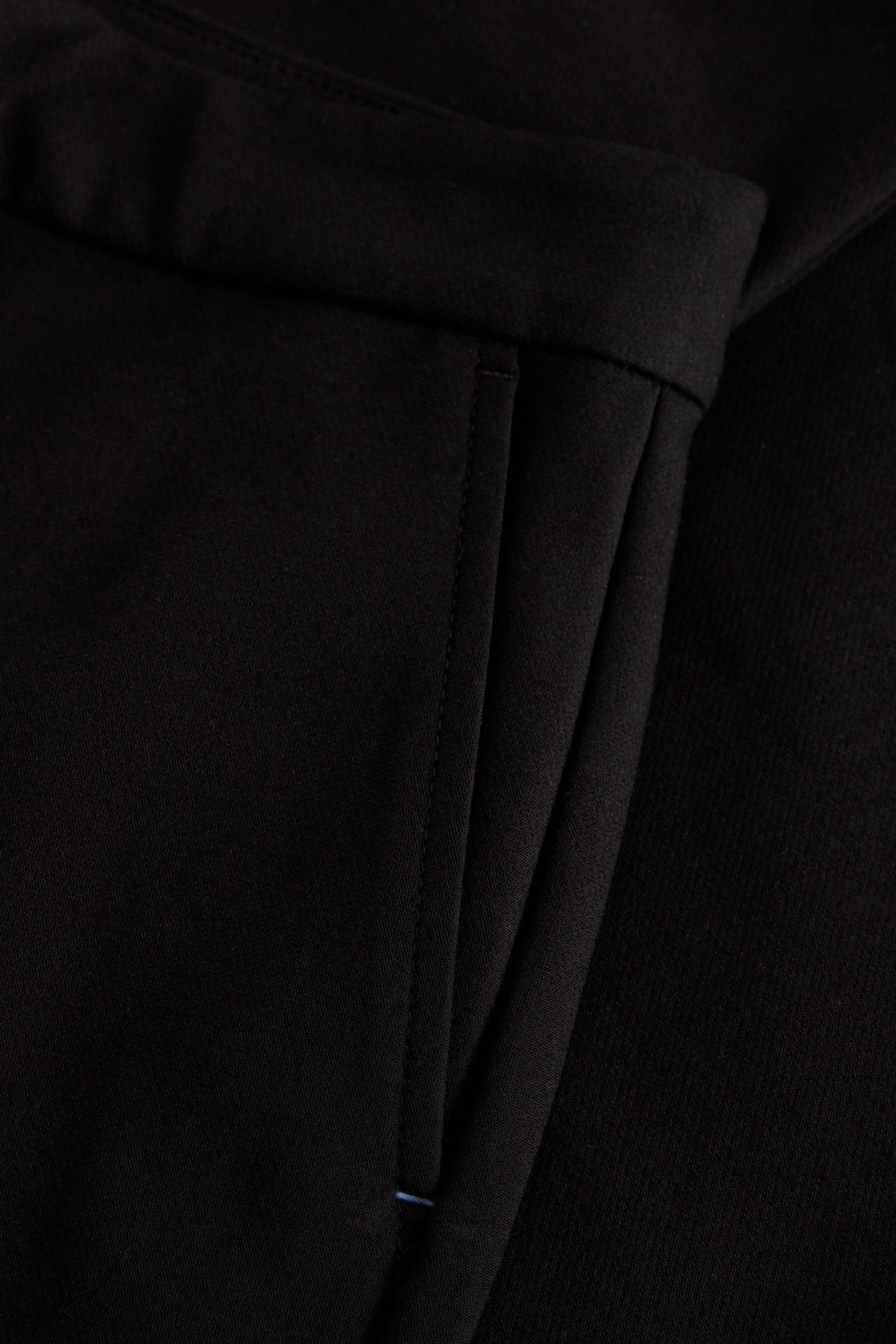Close-up detail of a black garment, showing a folded cuff or hem with a vertical seam and fine fabric texture.