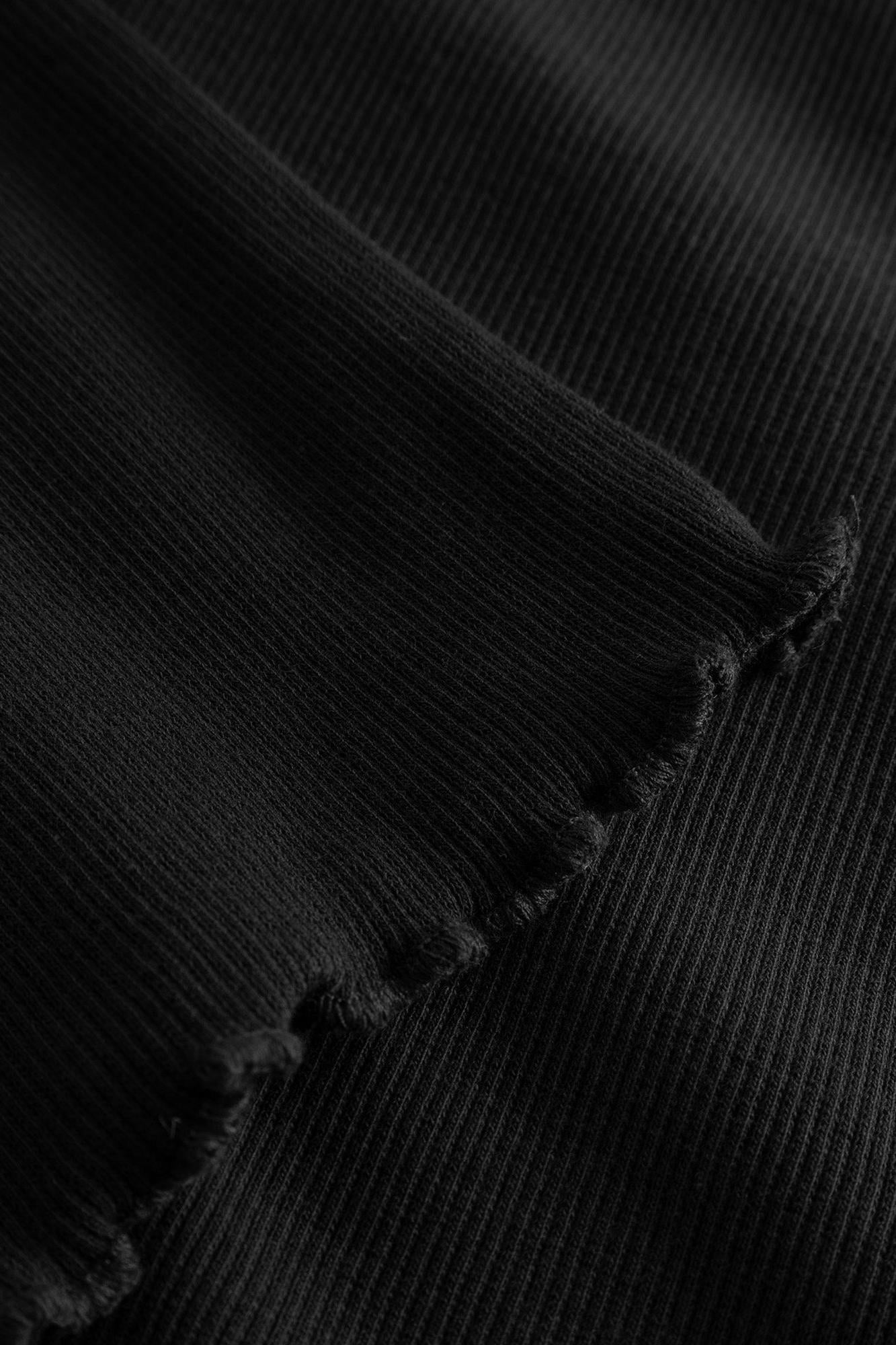 Close-up of a black ribbed knit fabric with a frayed edge, showing the texture and weave detail.