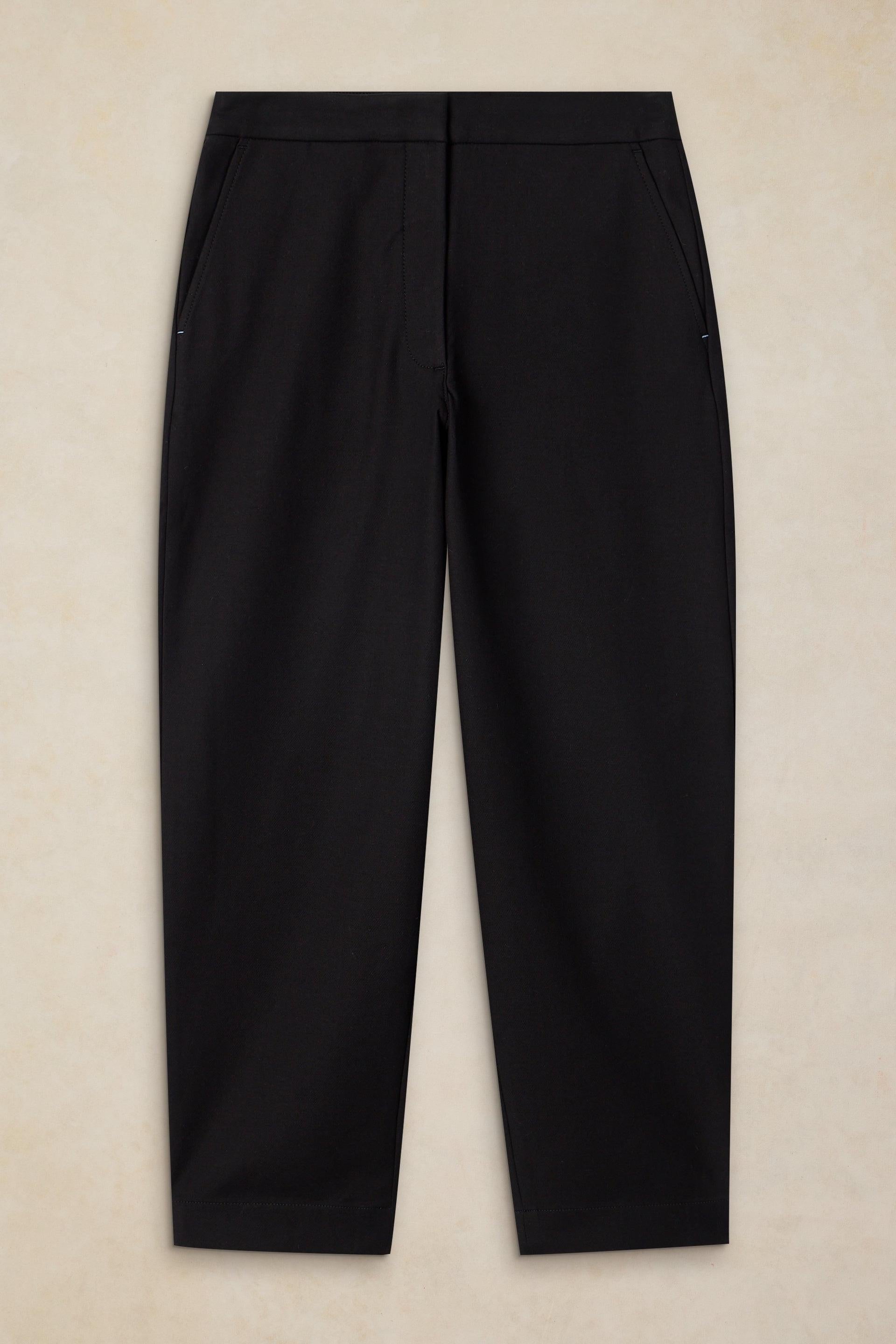 Black trousers laid flat against a light beige textured background.