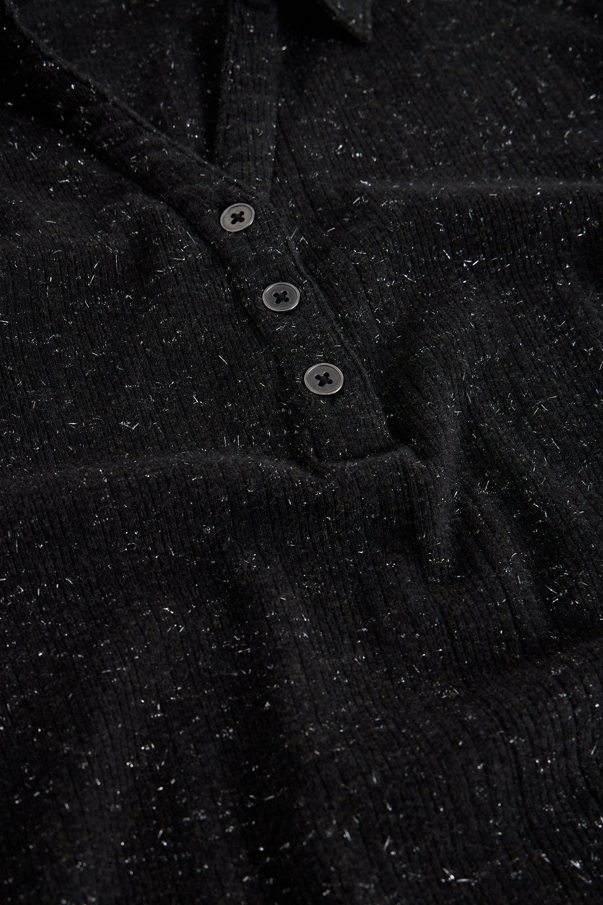 Close up of a black rib cotton polo top with silver sparkle detail and buttons.
