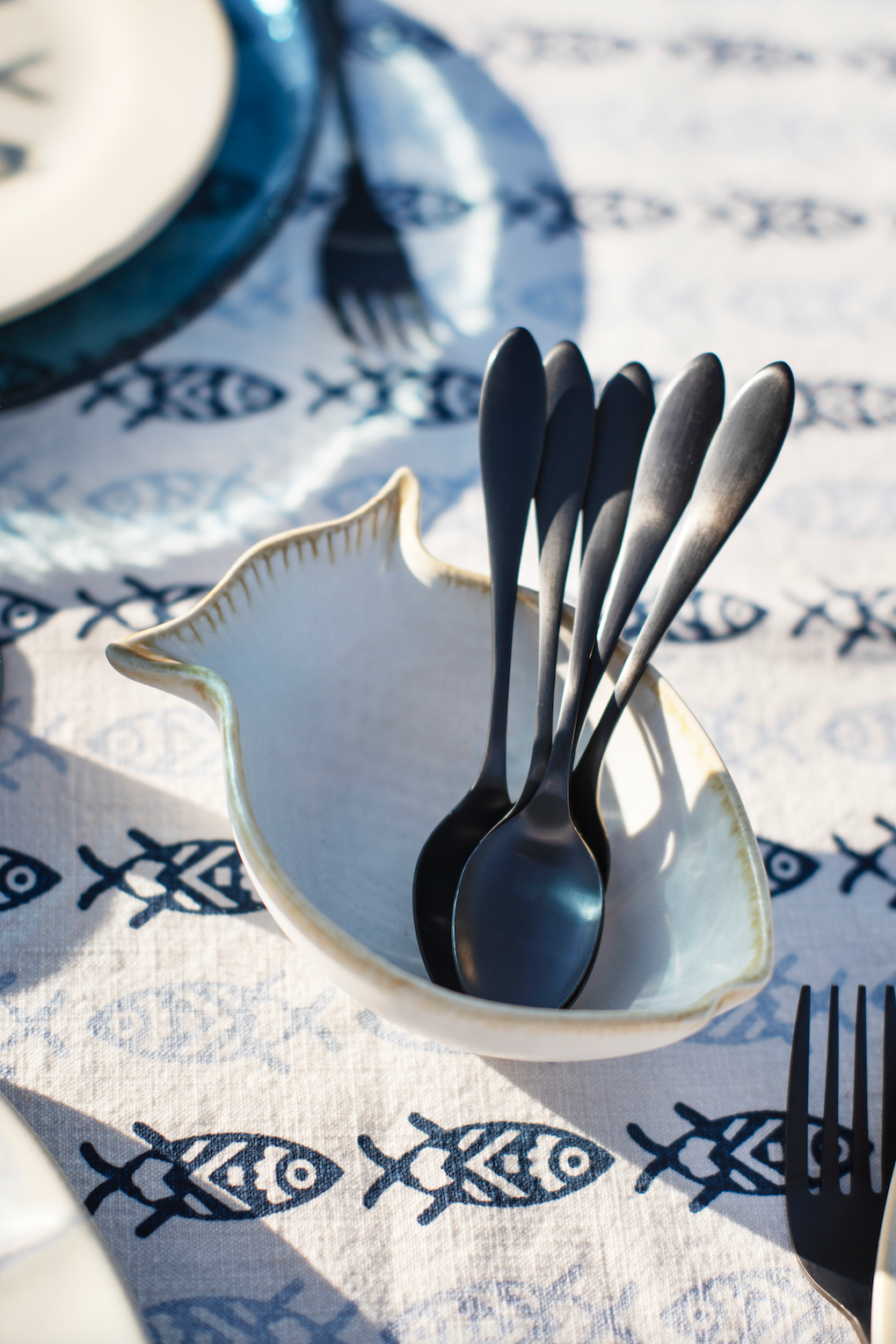 Black spoons in a ceramic fish-shaped bowl resting on a patterned cotton tablecloth.