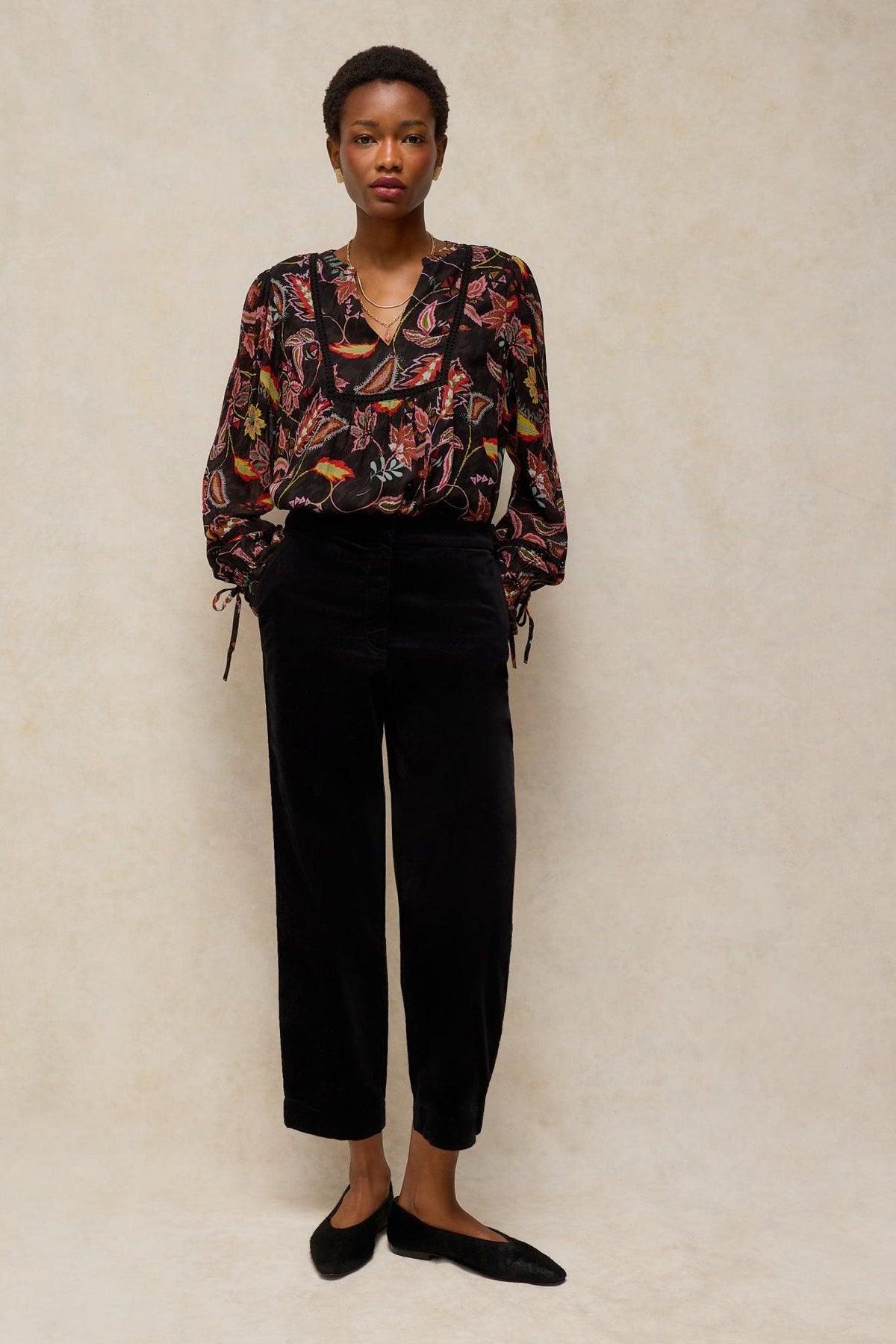 A model wearing a black White Stuff viscose floral print shirt with long sleeves and black trousers.