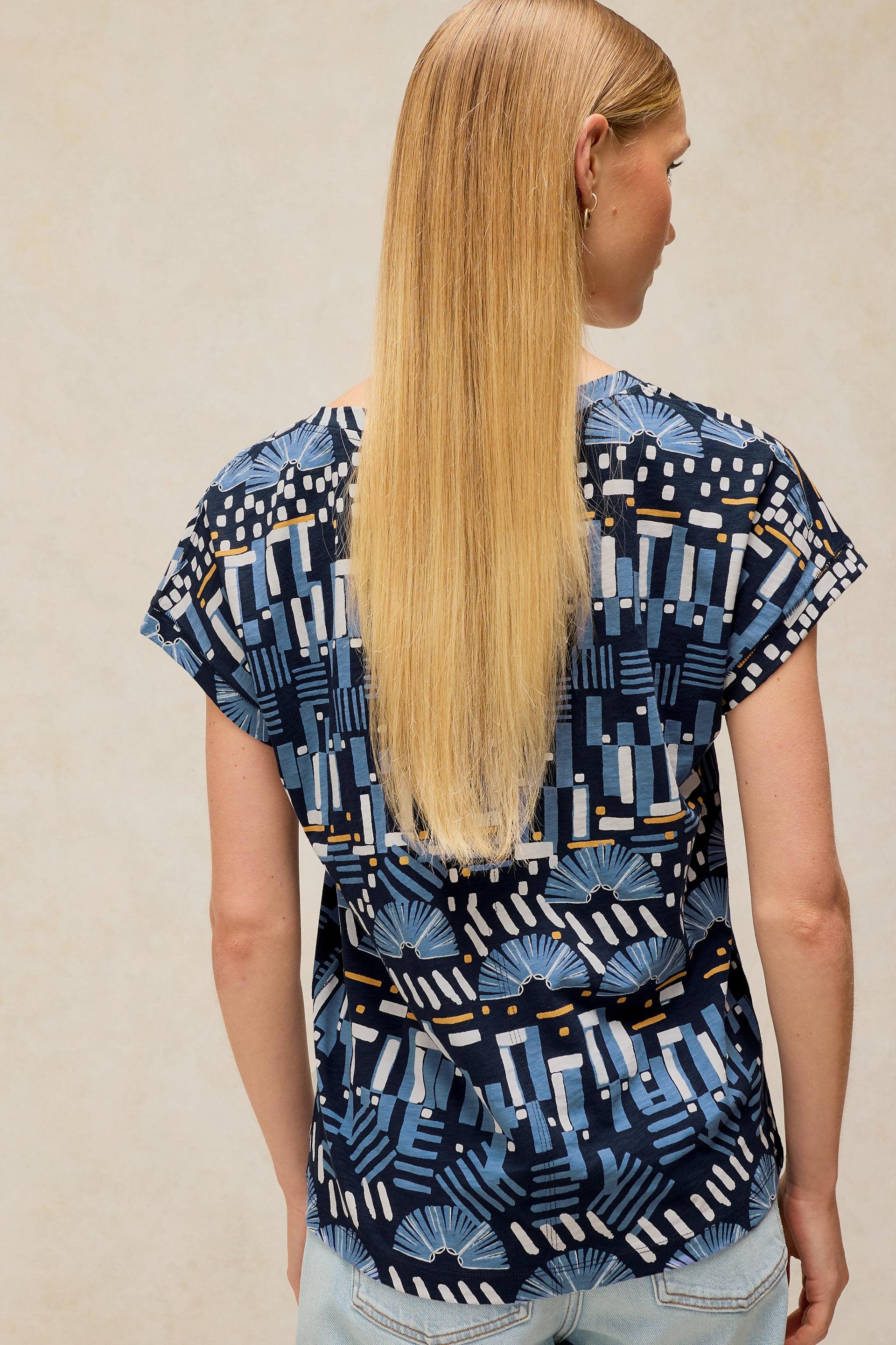 Woman with long blonde hair wearing a patterned blue cotton top seen from behind