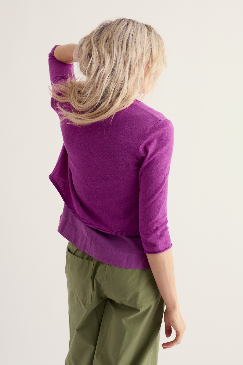 Blonde woman wearing a vibrant purple organic cotton cardigan against a neutral studio background.