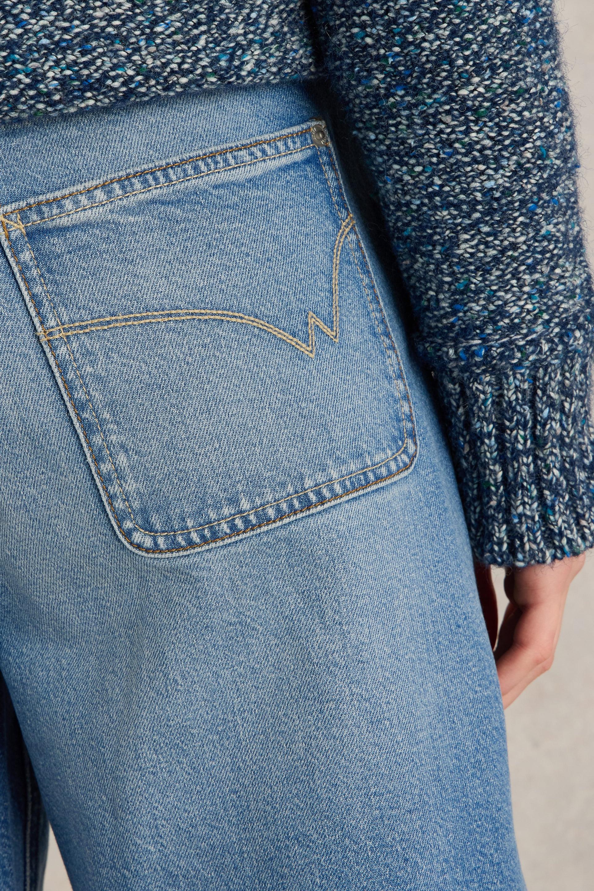 Close-up of light blue denim jeans with a textured pocket and a navy blue chunky knit sweater