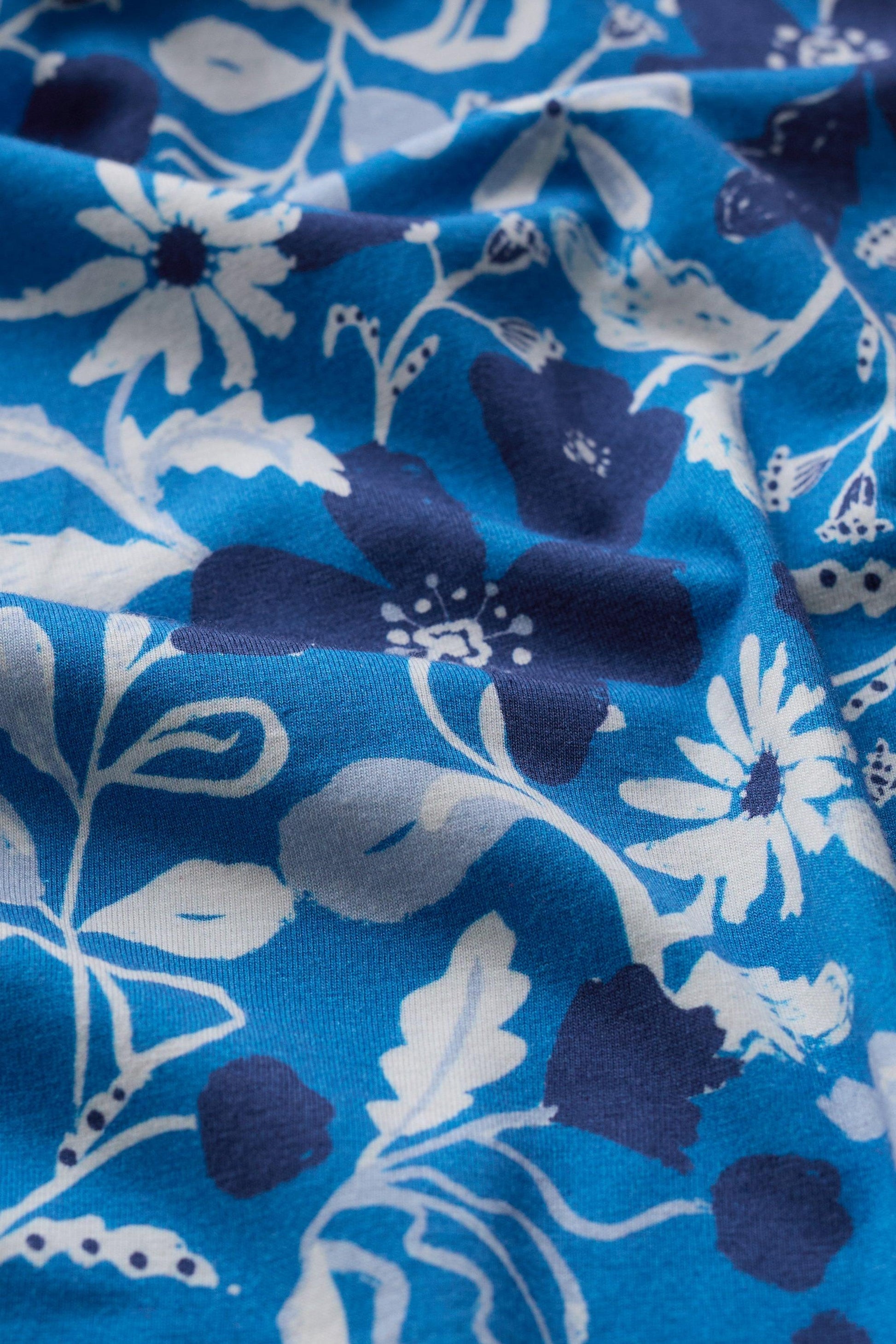 Close-up of soft blue fabric with a white and dark blue floral pattern in folds.