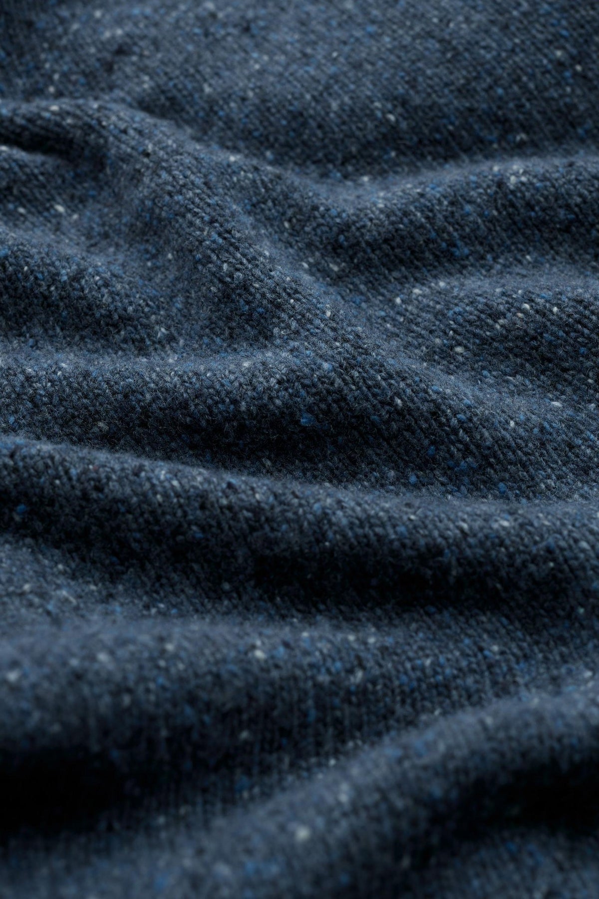 Close up fabric texture of a soft blue merino wool men's sweater with subtle flecks.