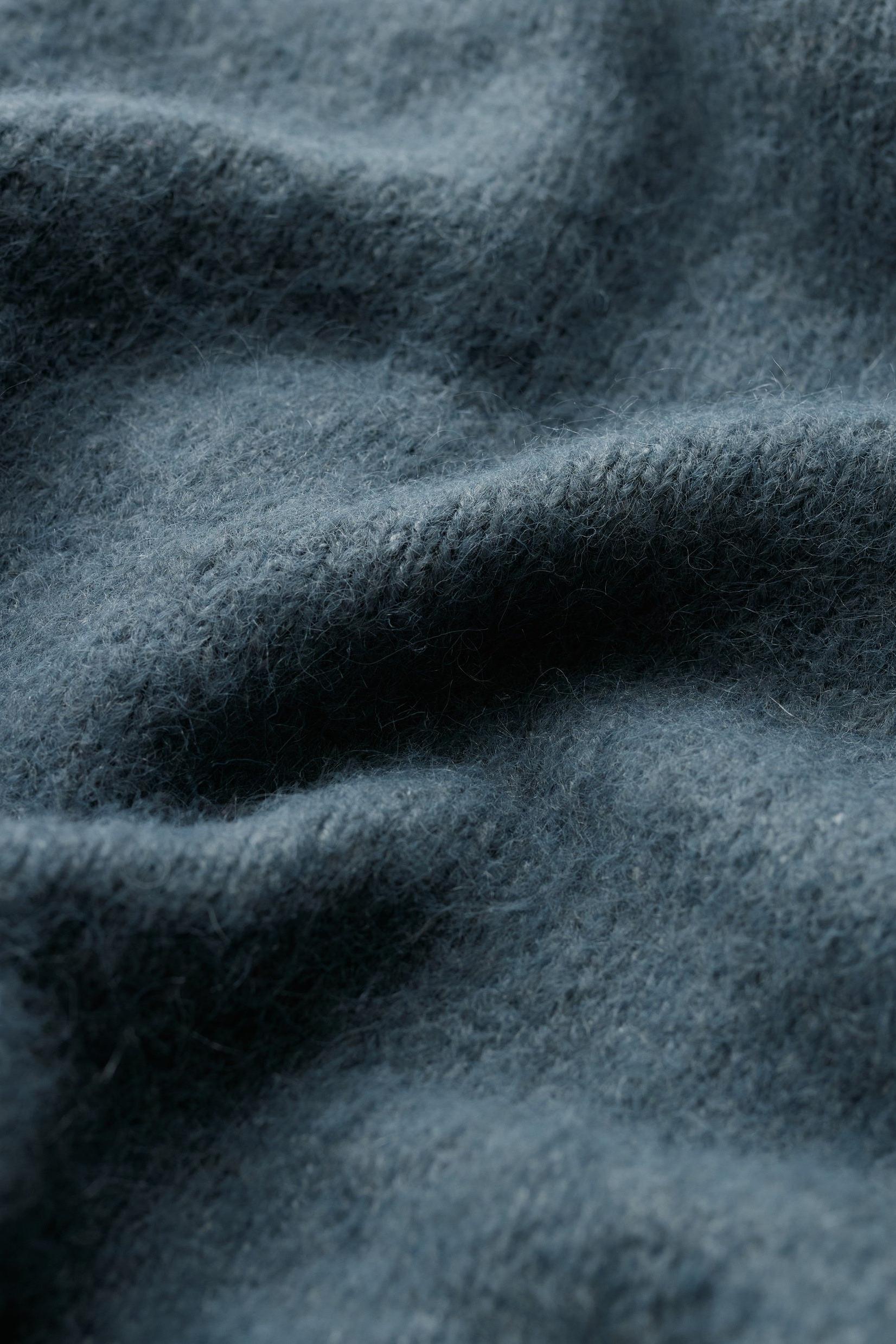 Close-up of a soft blue mohair cardigan fabric with a textured knit surface.