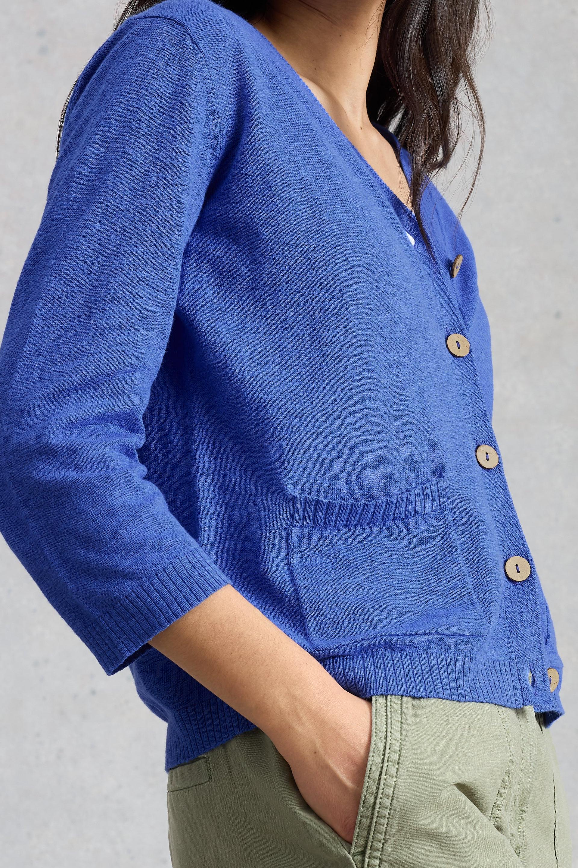 Person wearing a bright blue organic cotton cardigan with wooden buttons and pockets.
