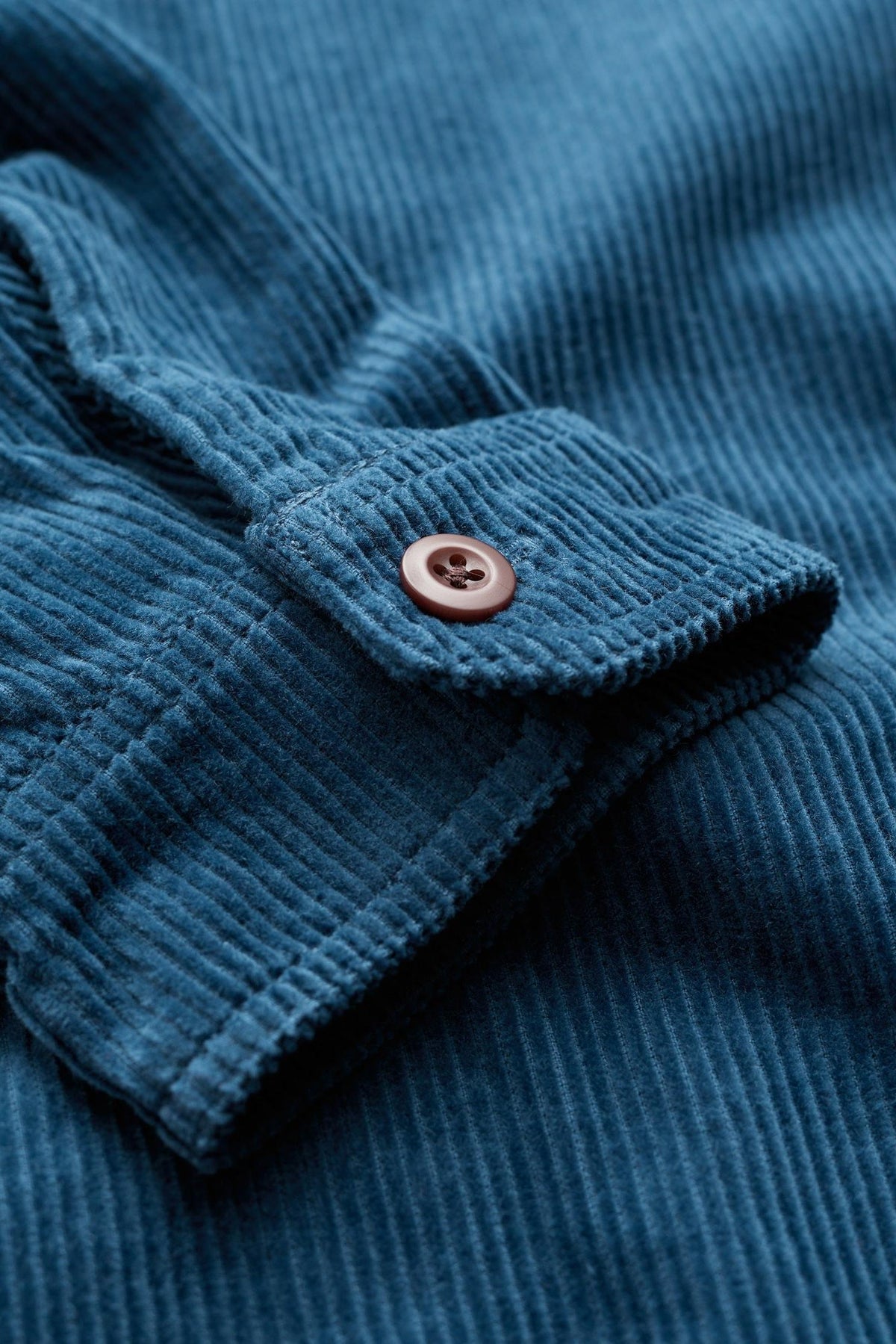 Close-up of a blue organic cotton corduroy sleeve cuff with a button on a Seasalt Cornwall men's shirt.