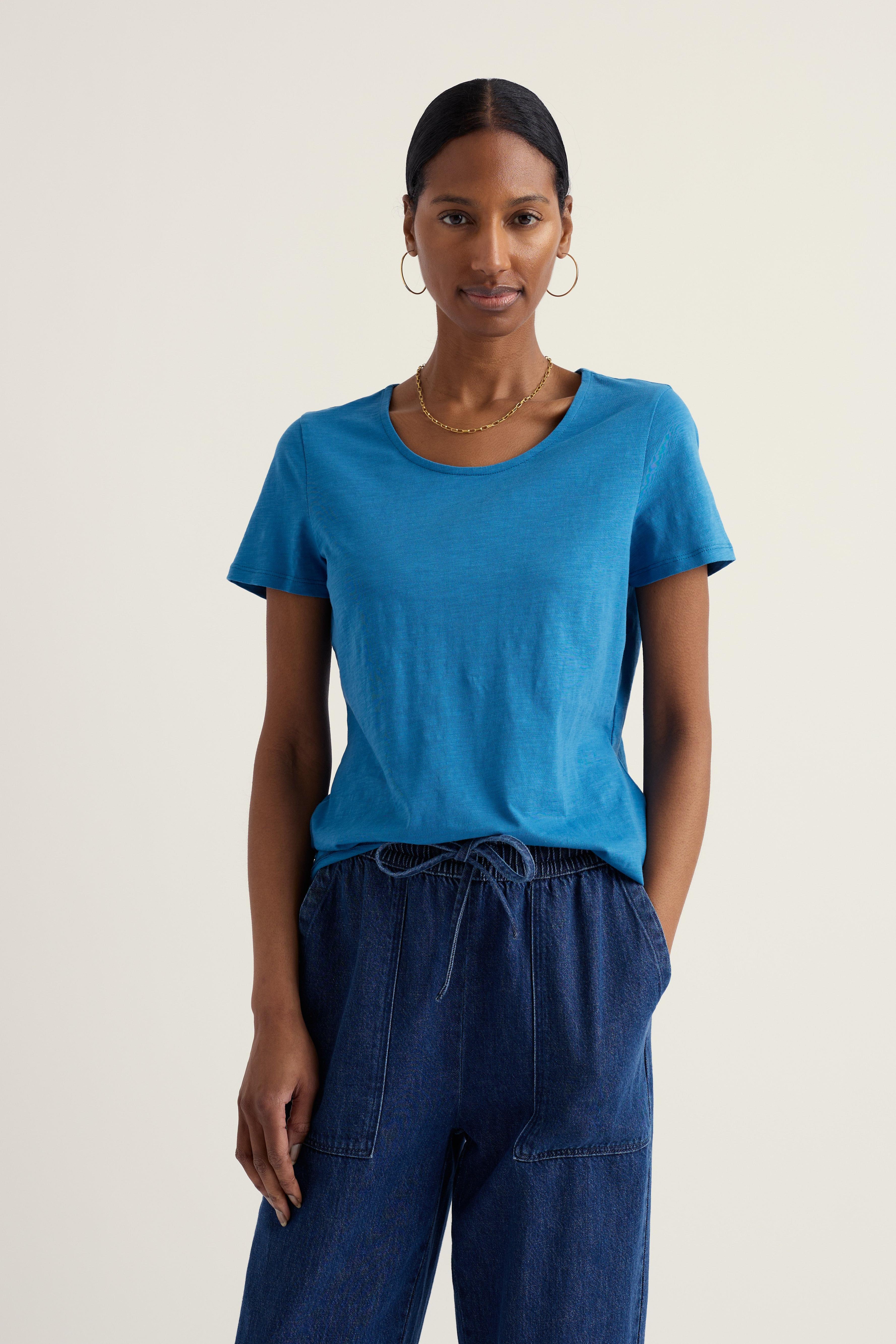 Woman wearing a blue organic cotton t-shirt and dark blue pants on a plain background