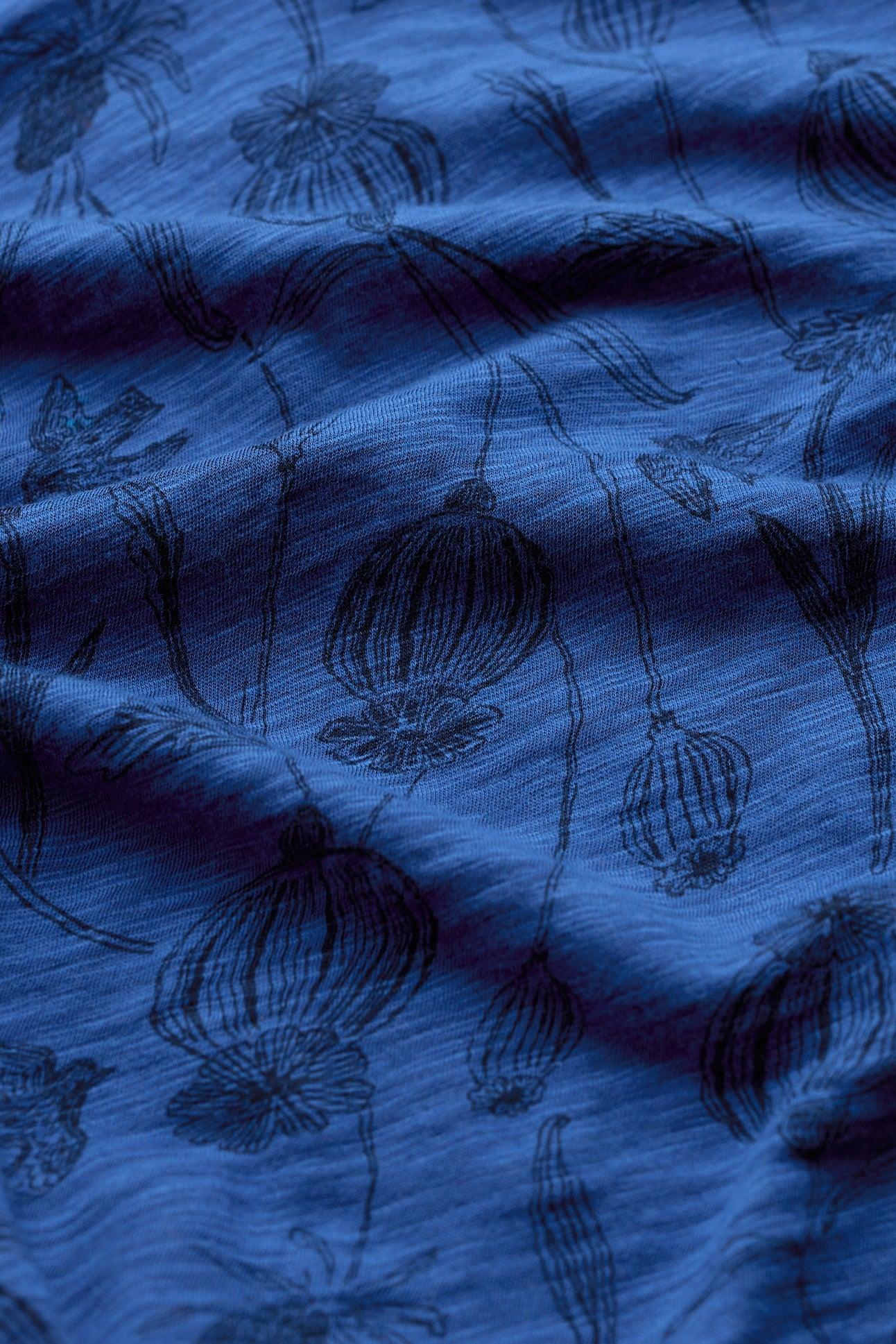 Close-up of a blue organic cotton shirt with black botanical poppy print and soft folds.
