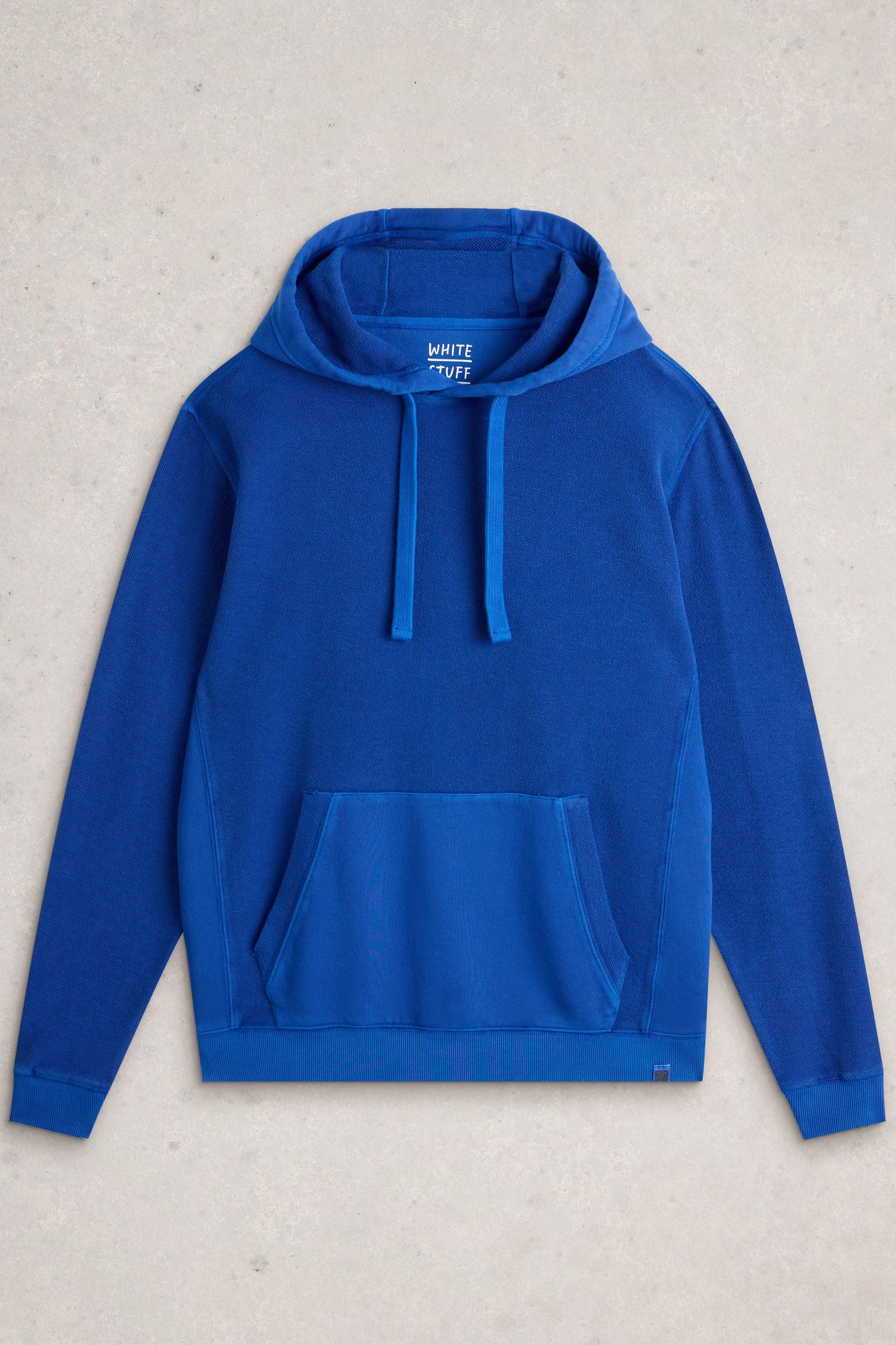 A bright blue pullover hoodie with a drawstring hood and front kangaroo pocket, laid flat on a light gray textured background. The brand name 'WHITE STUFF' is visible on the inner neck label.