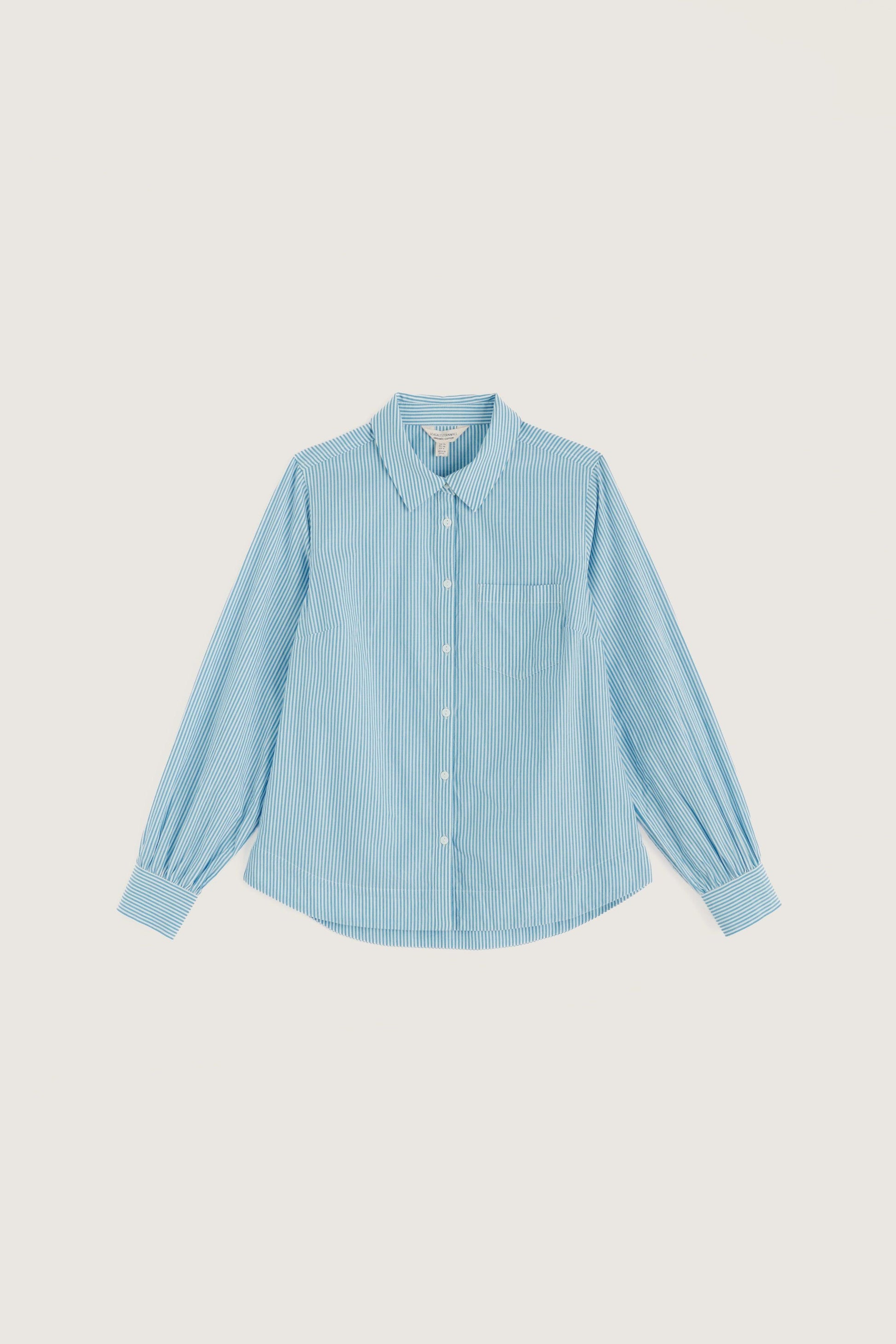 A light blue long-sleeve button-up shirt with a pointed collar, chest pocket, and gathered cuffs, displayed flat against a solid light beige background.