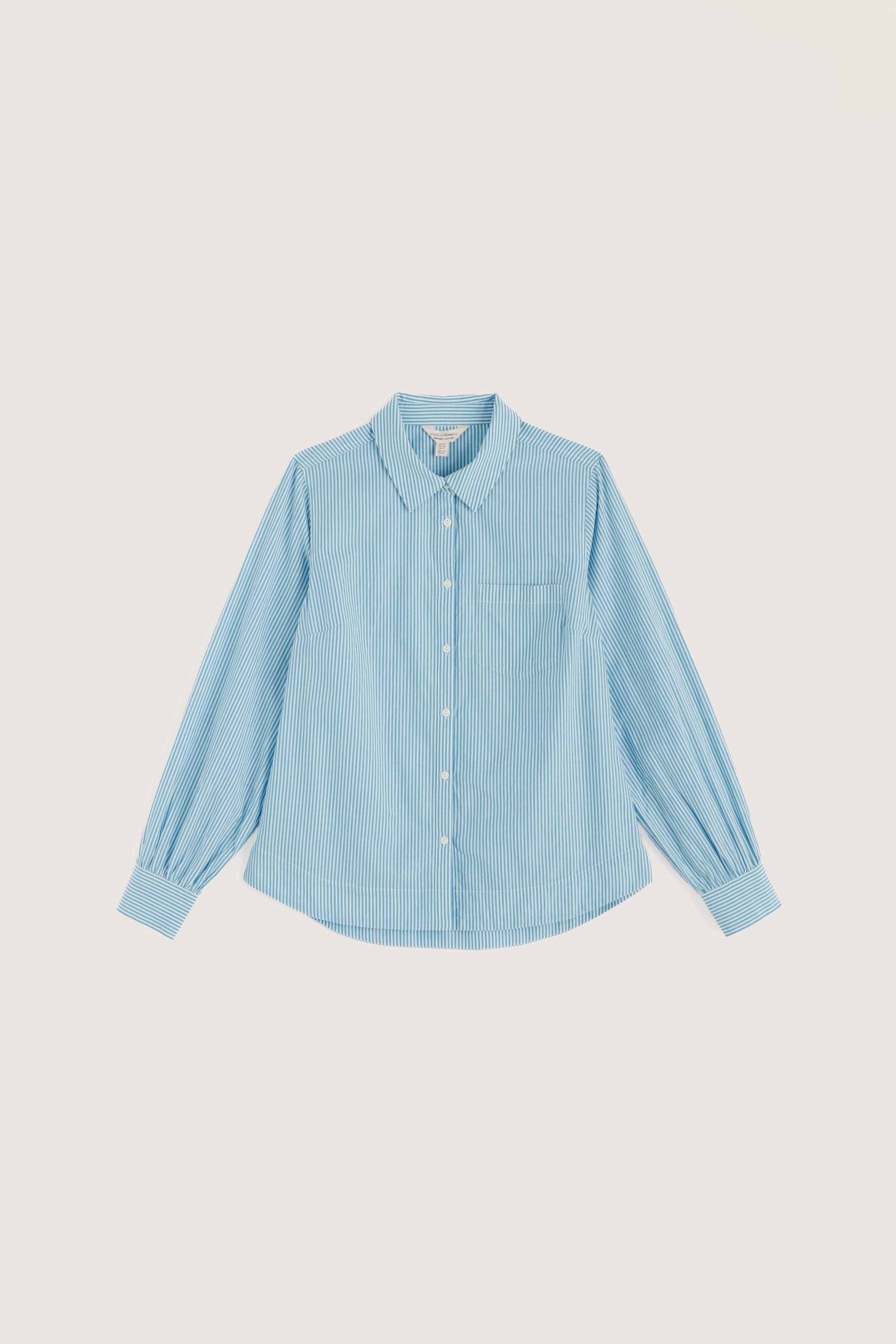 A light blue long-sleeve button-up shirt with a pointed collar, chest pocket, and gathered cuffs, displayed flat against a solid light beige background.