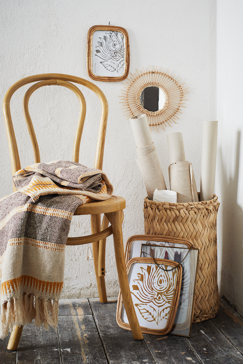Boho style wooden chair with a patterned throw blanket next to a wicker basket containing canvas rolls and framed art.
