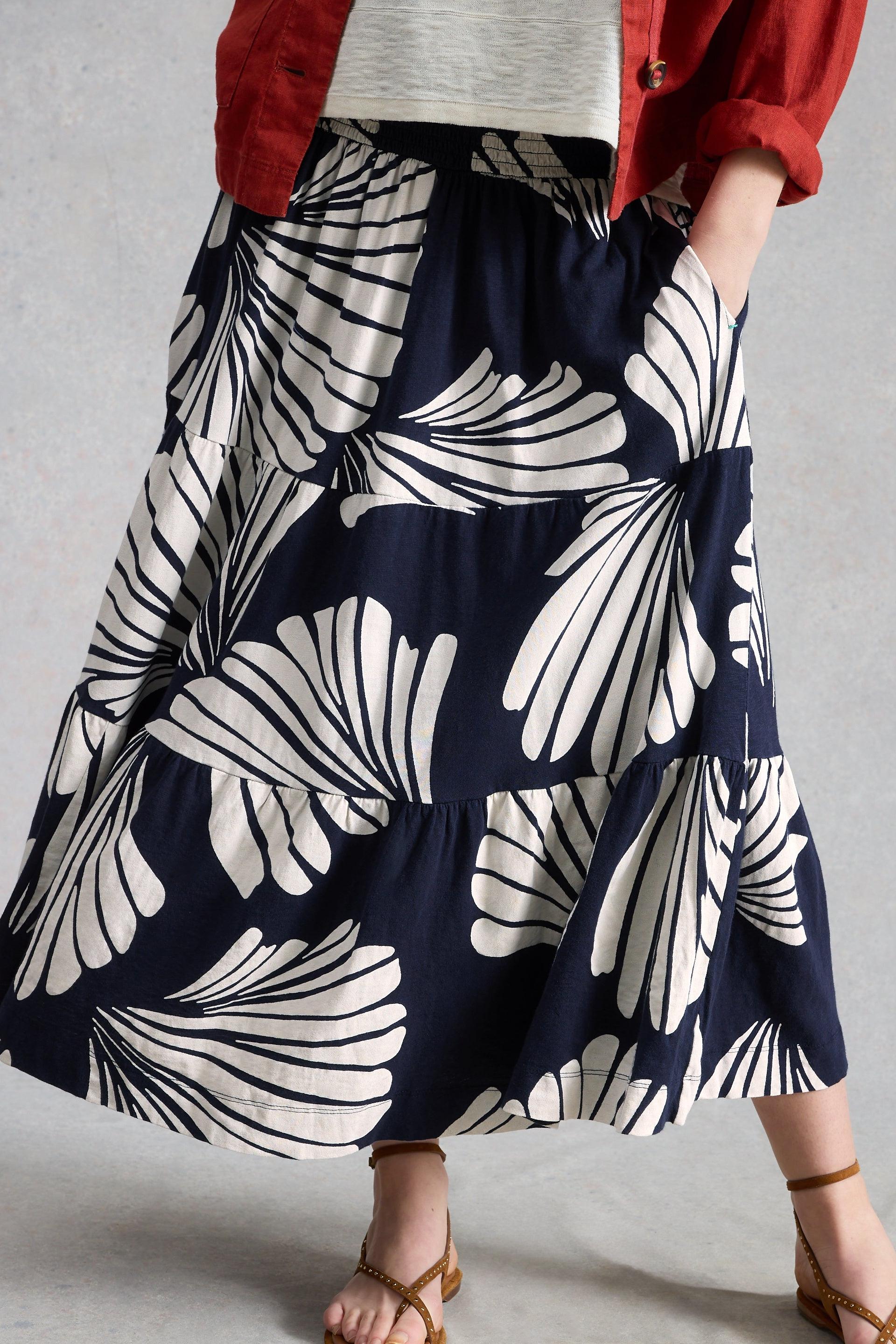 Person wearing a navy blue skirt with white abstract patterns and tiers on a gray background