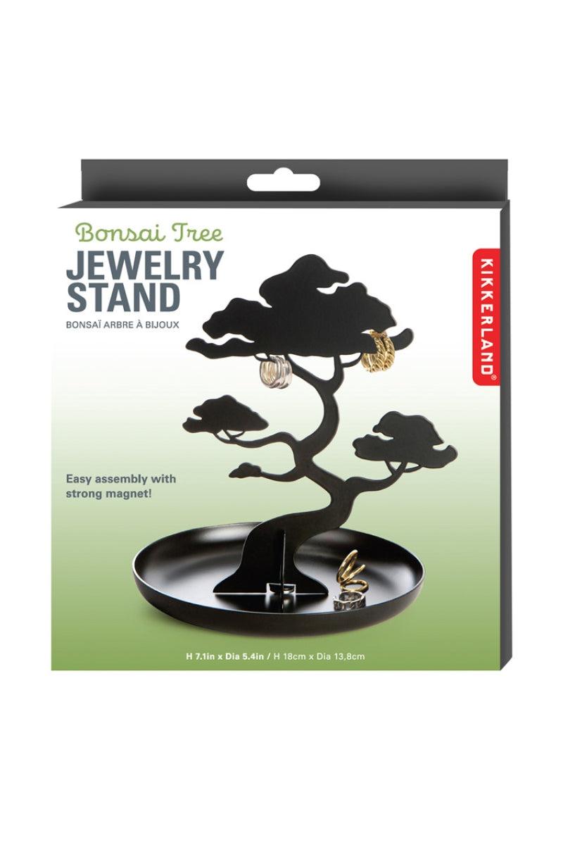 Kikkerland Bonsai Tree Jewelry Stand in its retail packaging, featuring a black metal bonsai tree display with a circular tray and hanging earrings shown on the box.