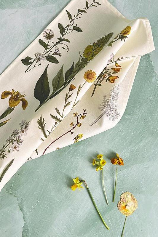 Floral-patterned tea towel on a textured green surface with dried flowers.
