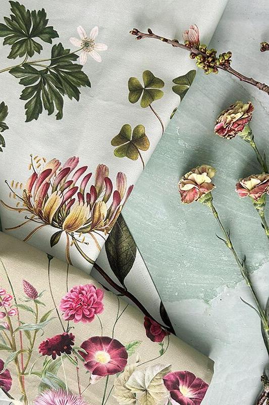 Rolls of floral-patterned cloth with green leaves and pink flowers on a light gray background.