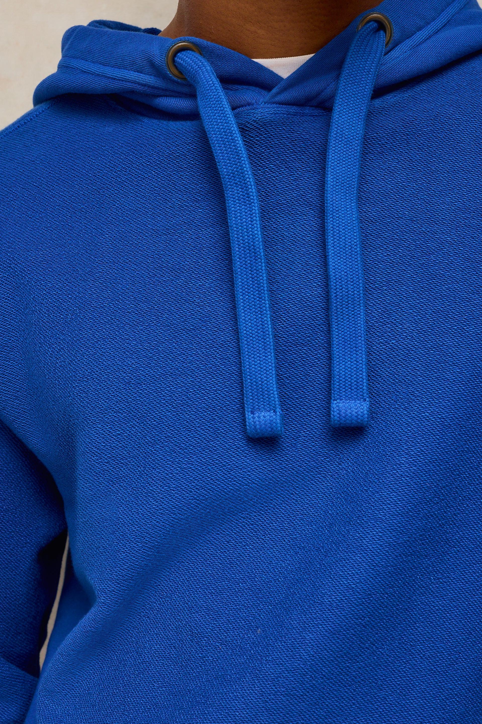 Close-up of a bright blue hooded sweatshirt with matching drawstrings and metal eyelets, worn by a person whose neck is visible at the top.