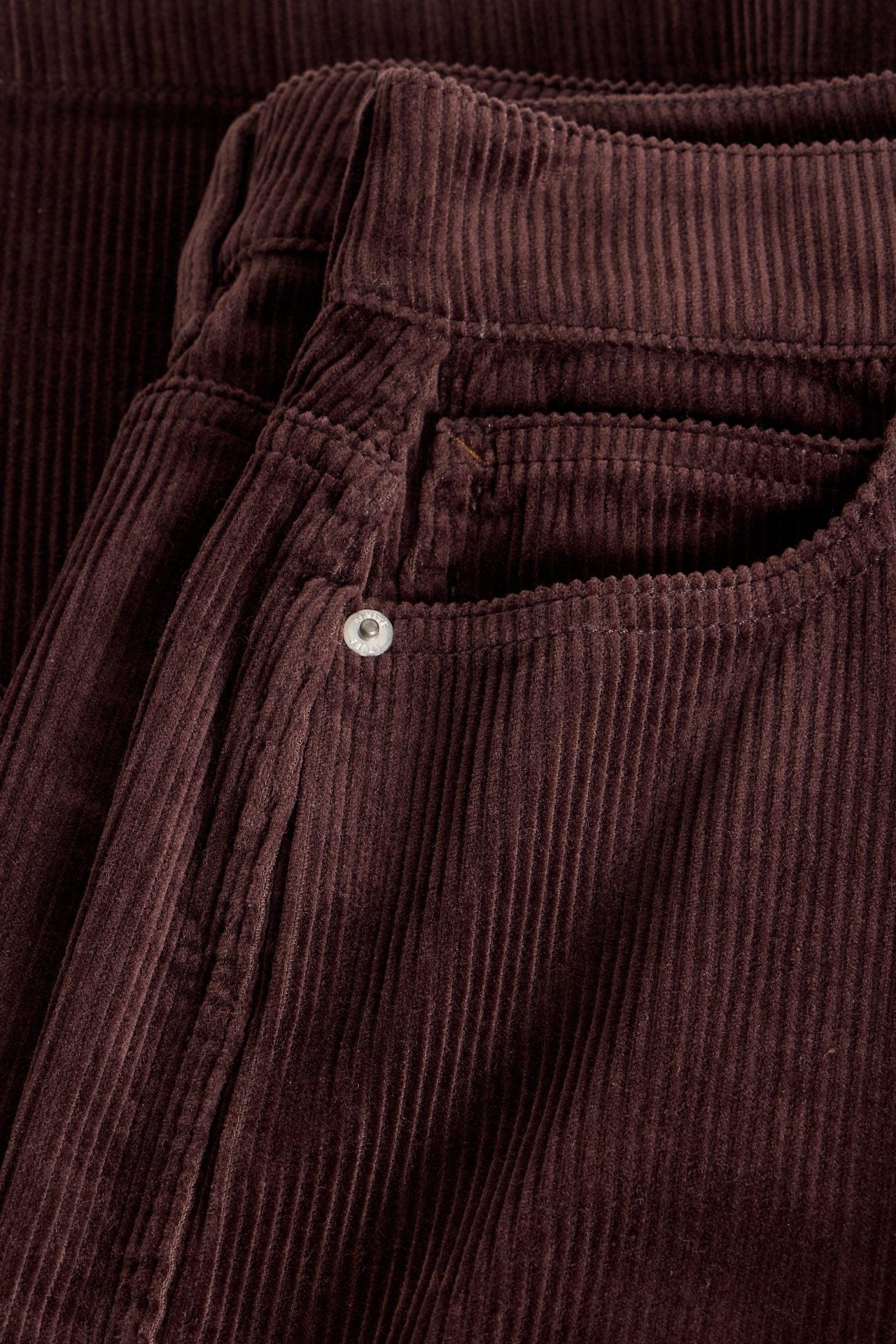 Close-up of brown cord trousers featuring a coin pocket and branded metal rivet by White Stuff.