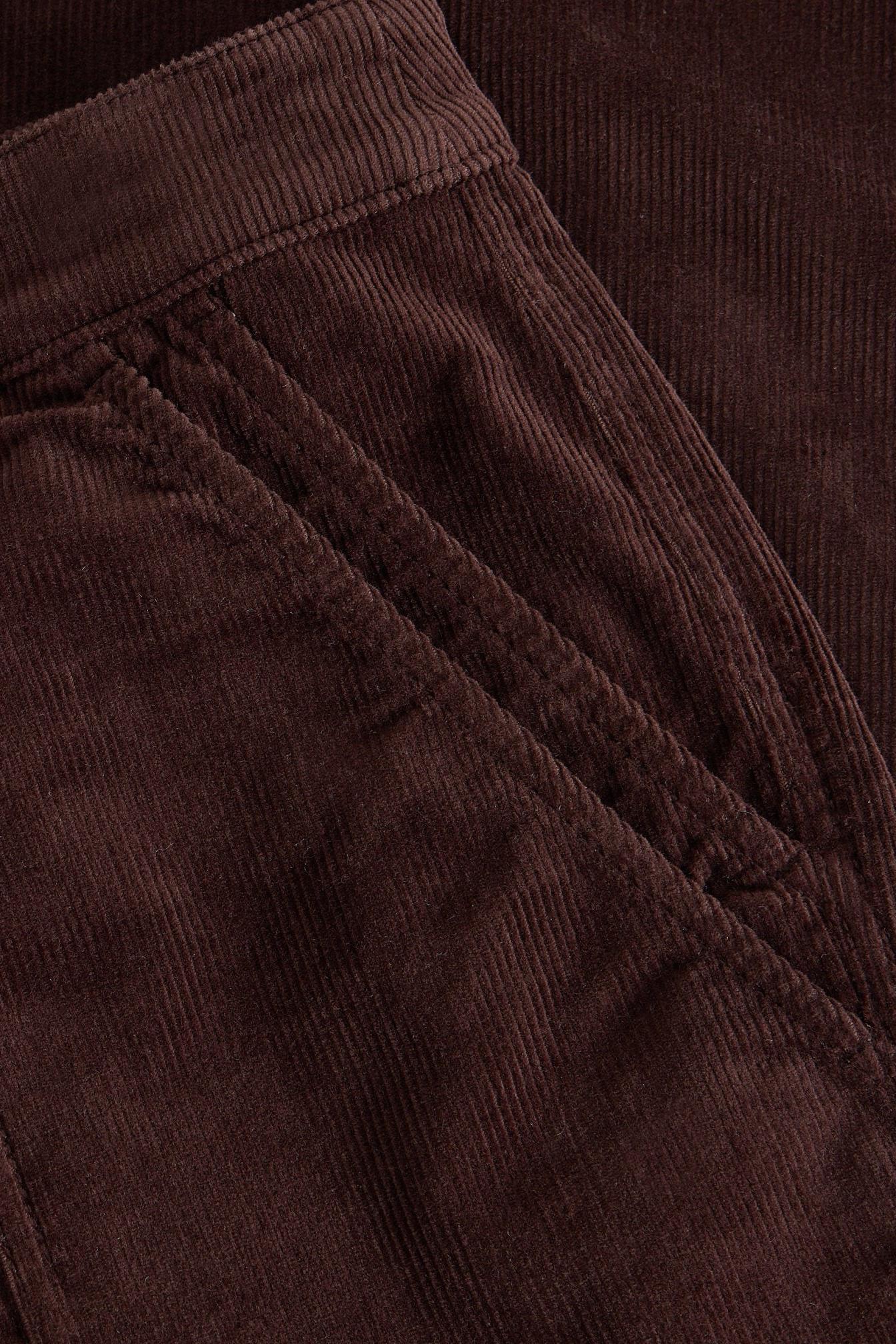 Close-up detail of a pocket on dark brown organic cotton corduroy trousers.