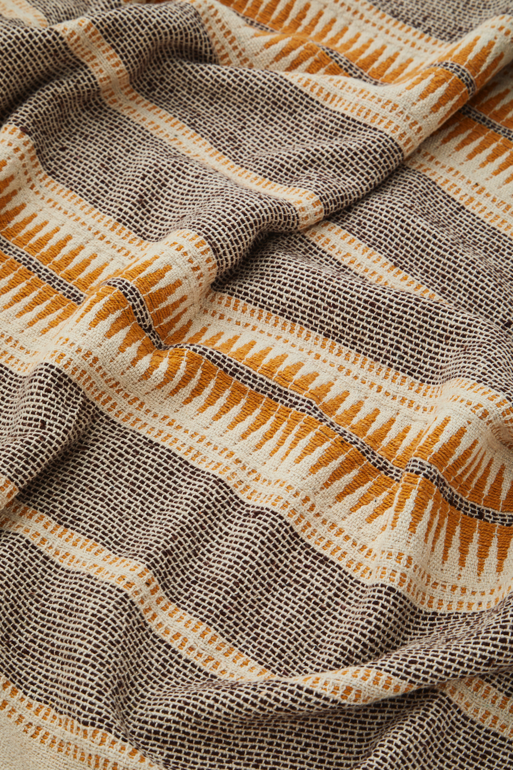 Close-up of a woven throw blanket with a brown and cream geometric tribal pattern and fringed texture.