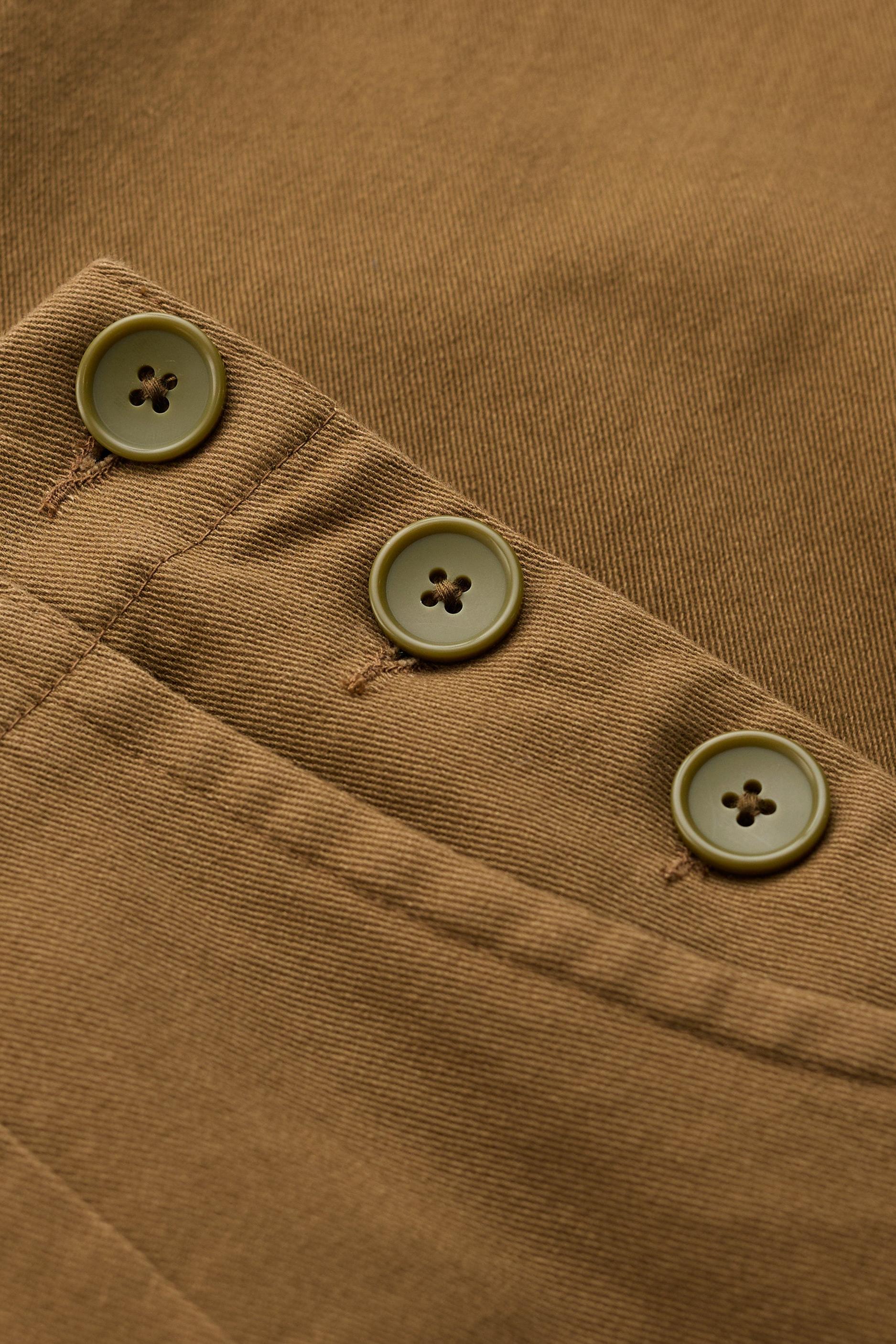 Close-up of a brown fabric garment showing a pocket corner with three round buttons.