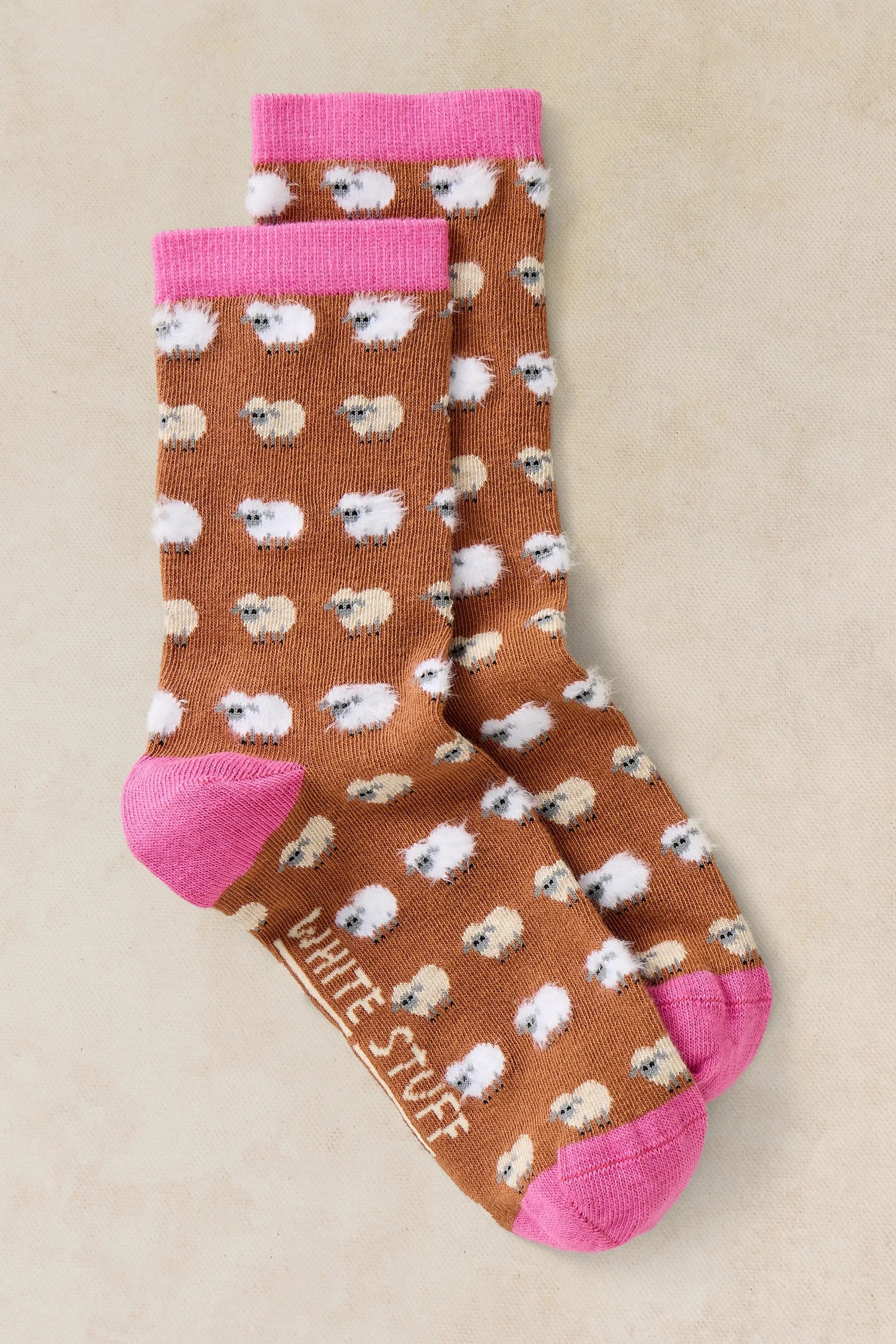 Pair of socks with sheep pattern and pink accents on a beige background