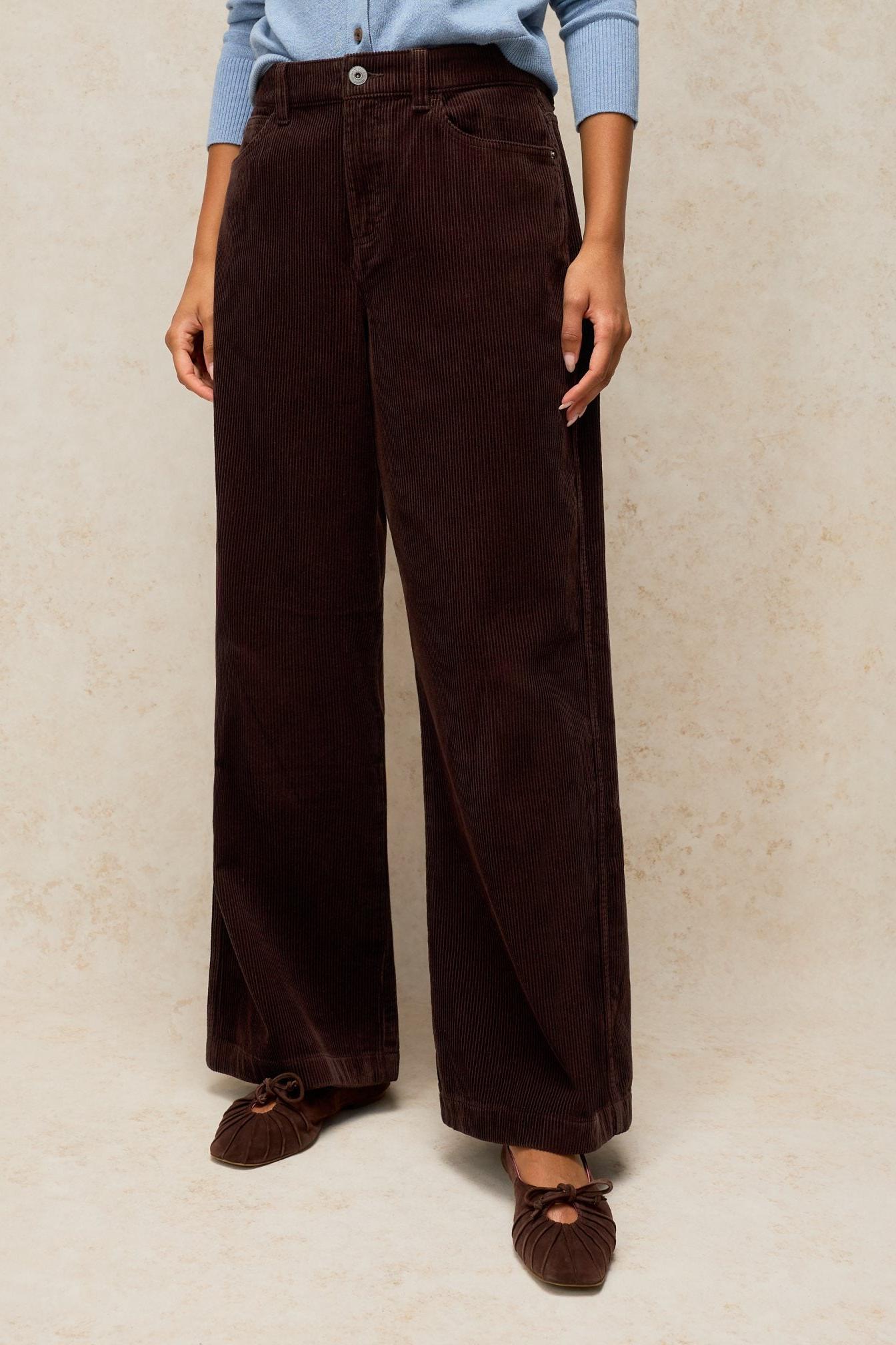 A person wearing brown wide-leg cord trousers from White Stuff against a neutral studio background.