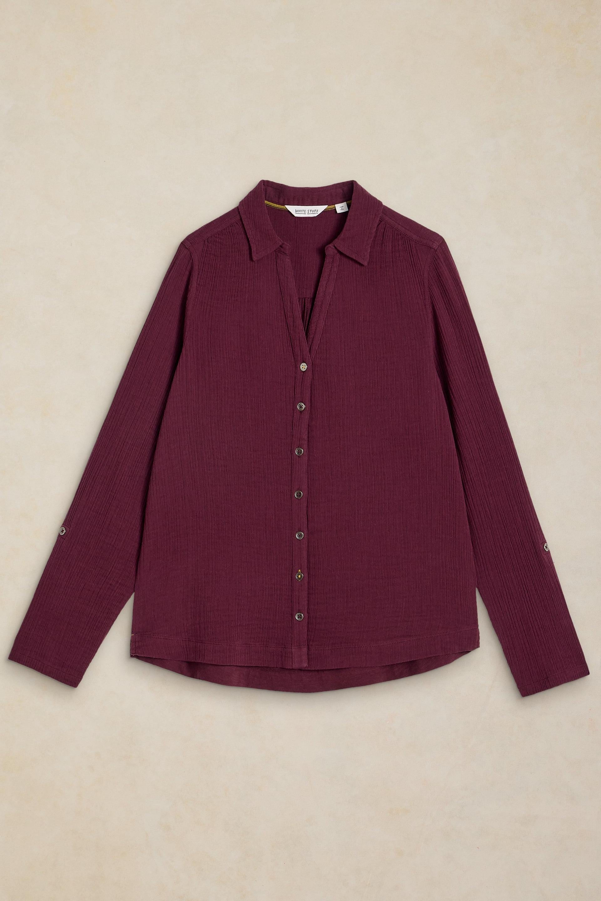 A long-sleeve button-up shirt in deep burgundy, laid flat against a textured beige background.