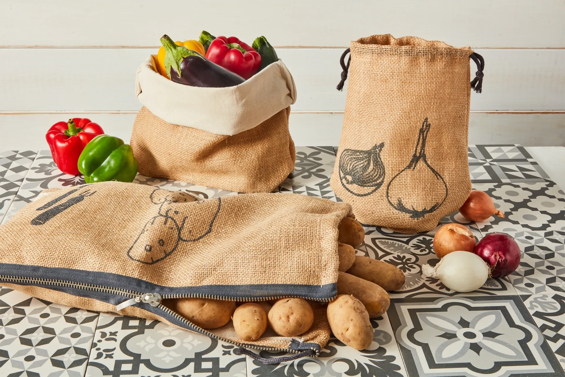 Set of reusable burlap bags with vegetable illustrations on a patterned surface.