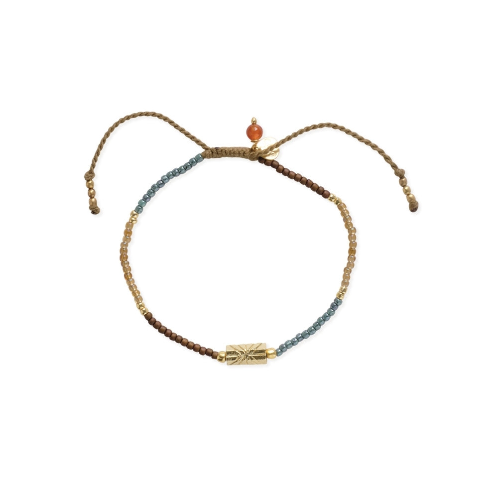 A delicate beaded bracelet featuring a carnelian gemstone and a gold textured charm on a cord.