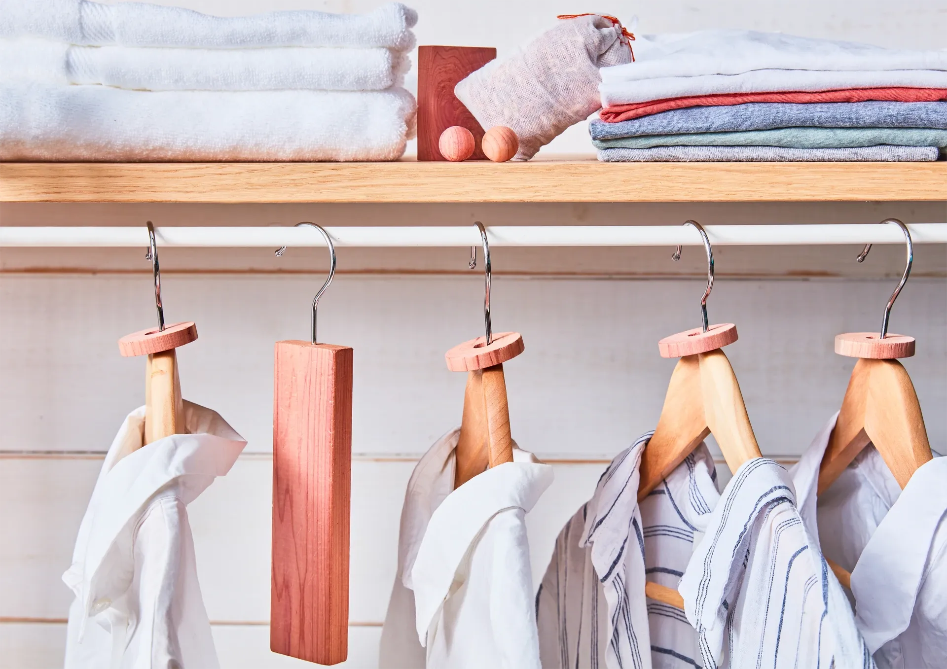Clothing on wooden hangers with folded clothes stacked above on a shelf.