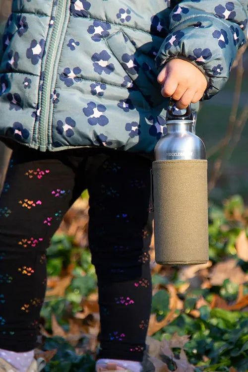 Person holding a metal water bottle with a textured sleeve outdoors