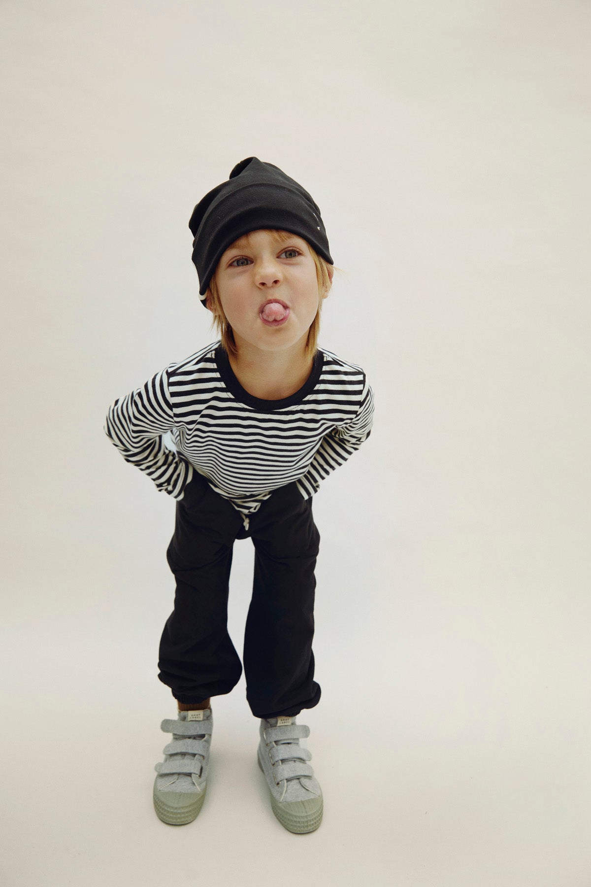 Child wearing a black and white striped shirt, black pants, and gray shoes on a plain background