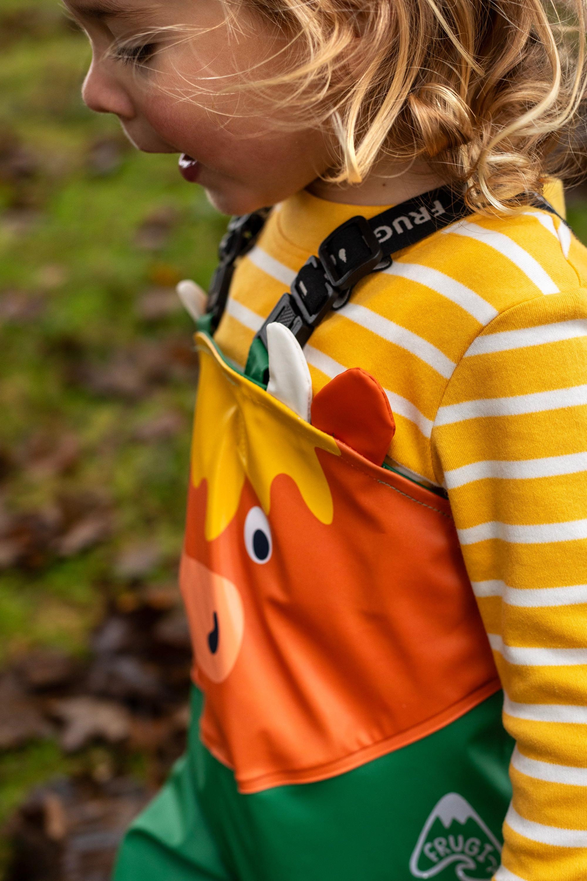 A young child wearing colorful Frugi animal print overalls and a striped yellow shirt outdoors