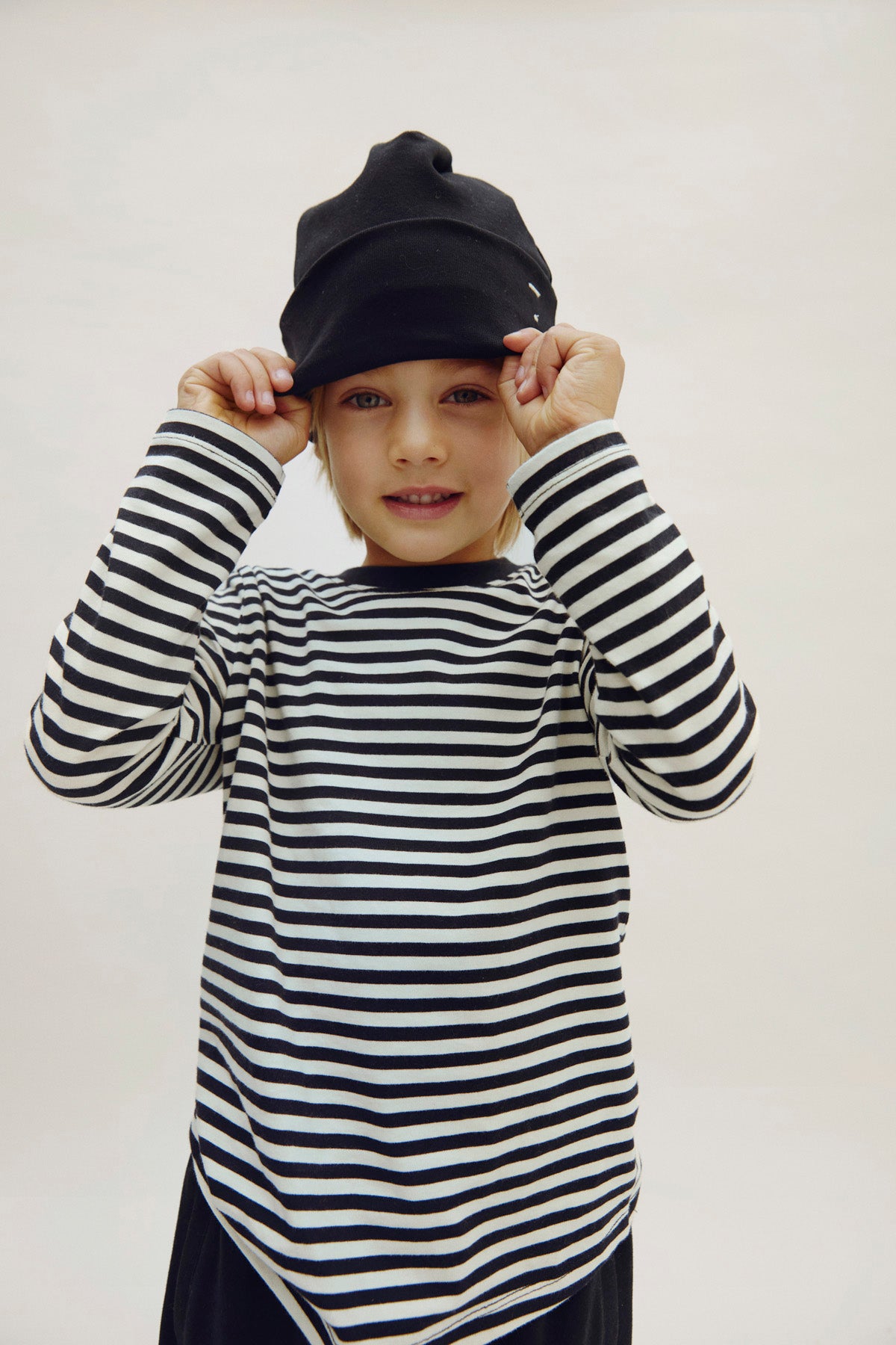 Child wearing a black and white striped shirt and black cap on a plain background