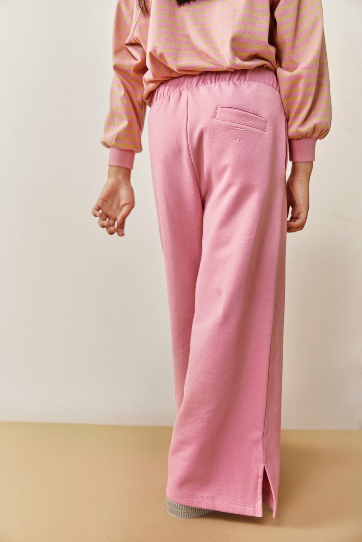 Person wearing a pink sweatshirt and pink sweatpants on a beige background