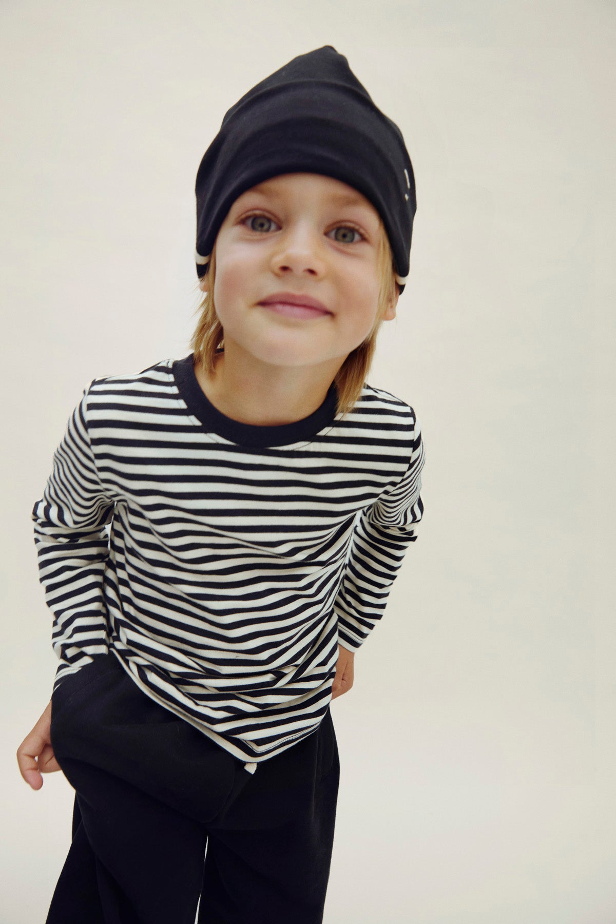 Child wearing a black and white striped shirt with a black beanie against a plain background