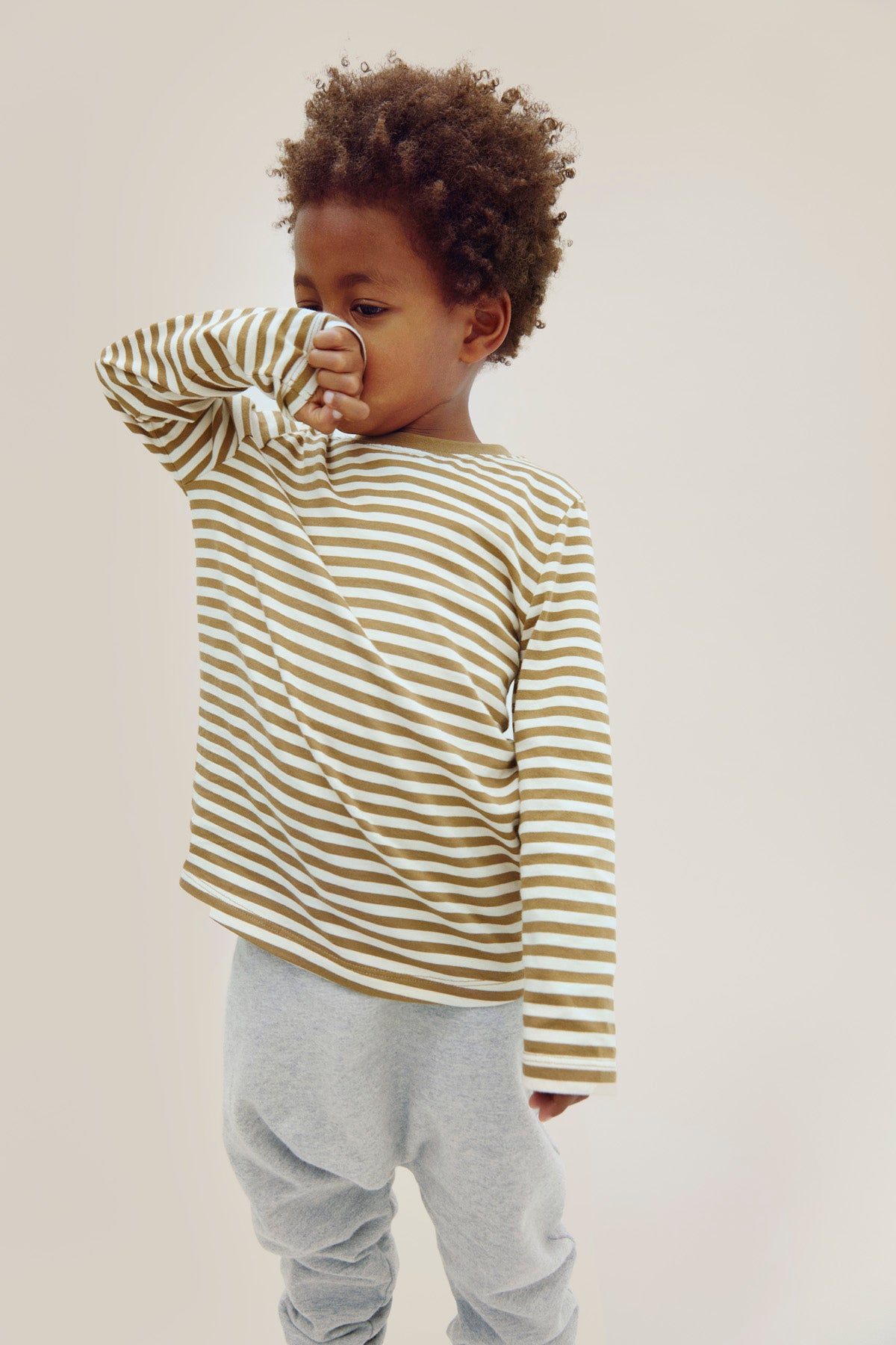 Child wearing a striped long-sleeve shirt and gray pants on a plain background