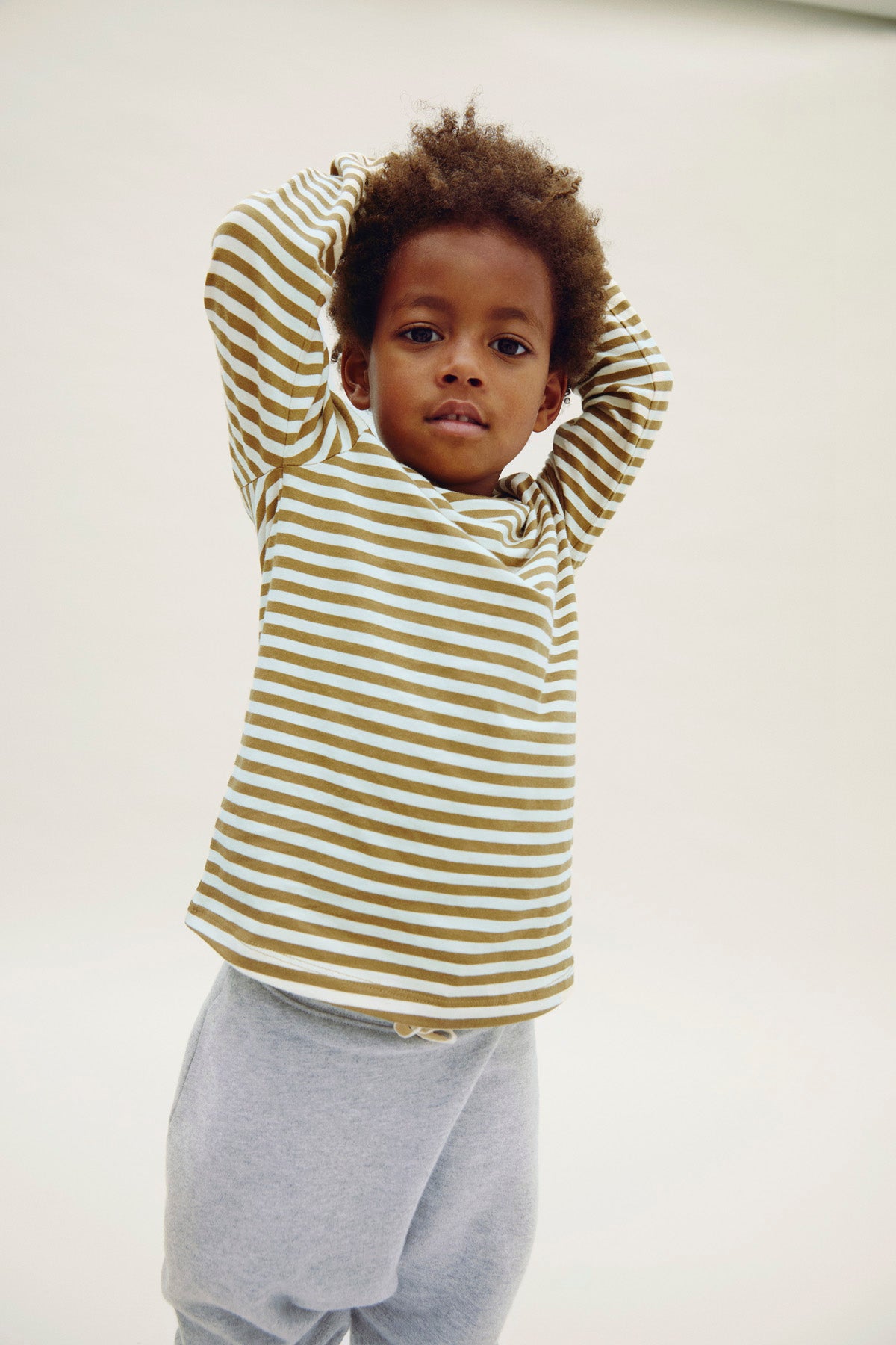 Child wearing a striped organic cotton shirt and gray pants against a white background