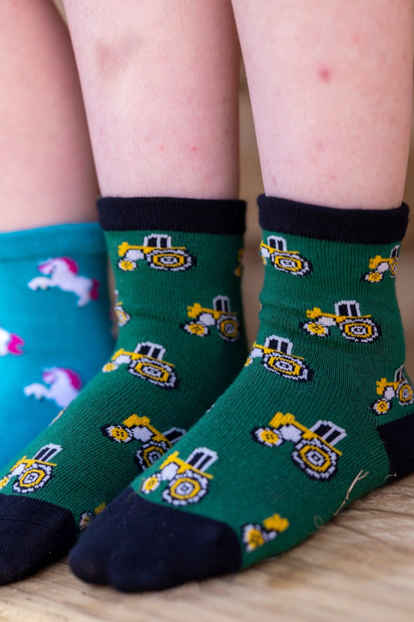 Two children wearing green tractor socks and blue unicorn socks standing on a wooden surface.